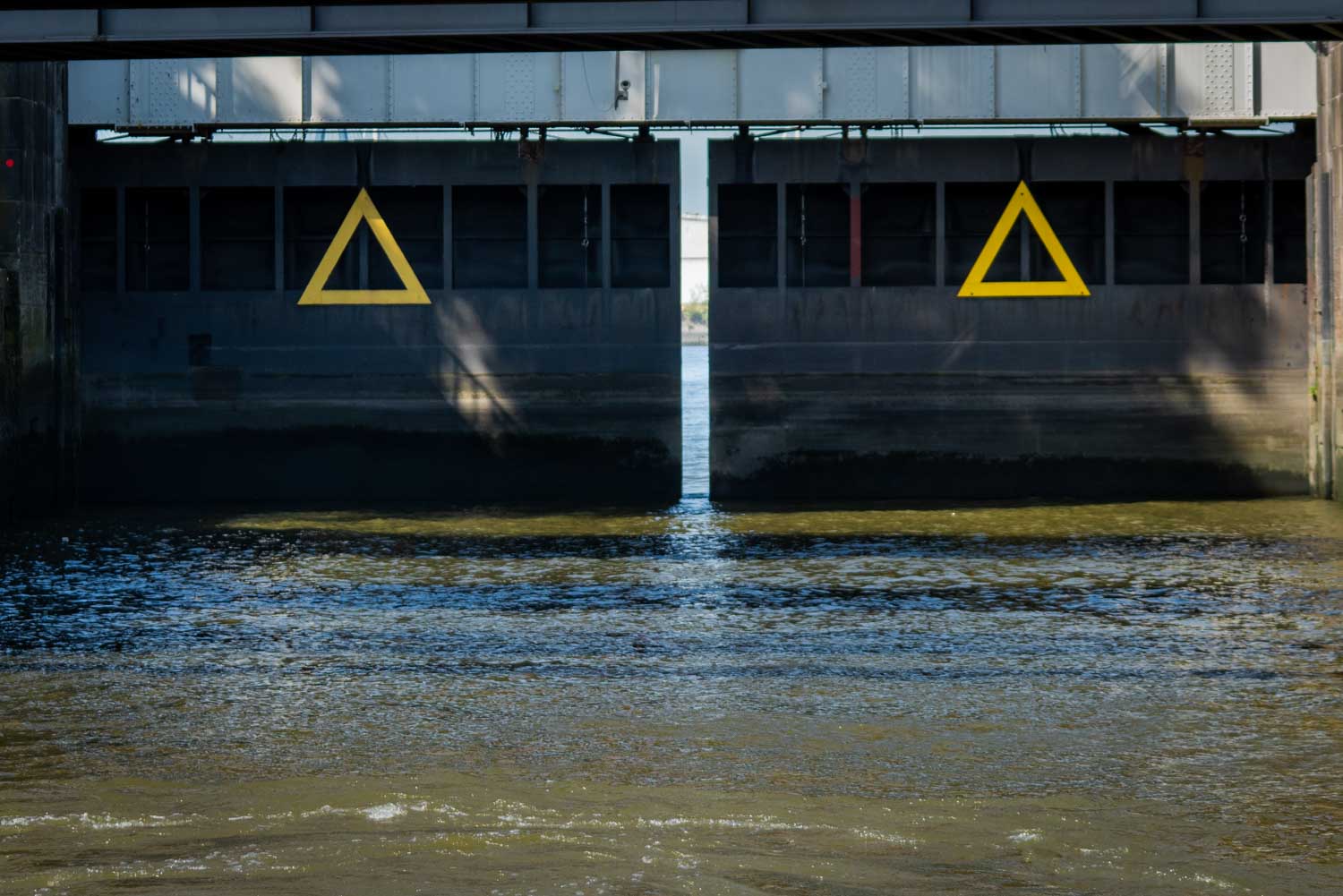 Closed metal lock gates over a waterway with yellow triangle symbols.