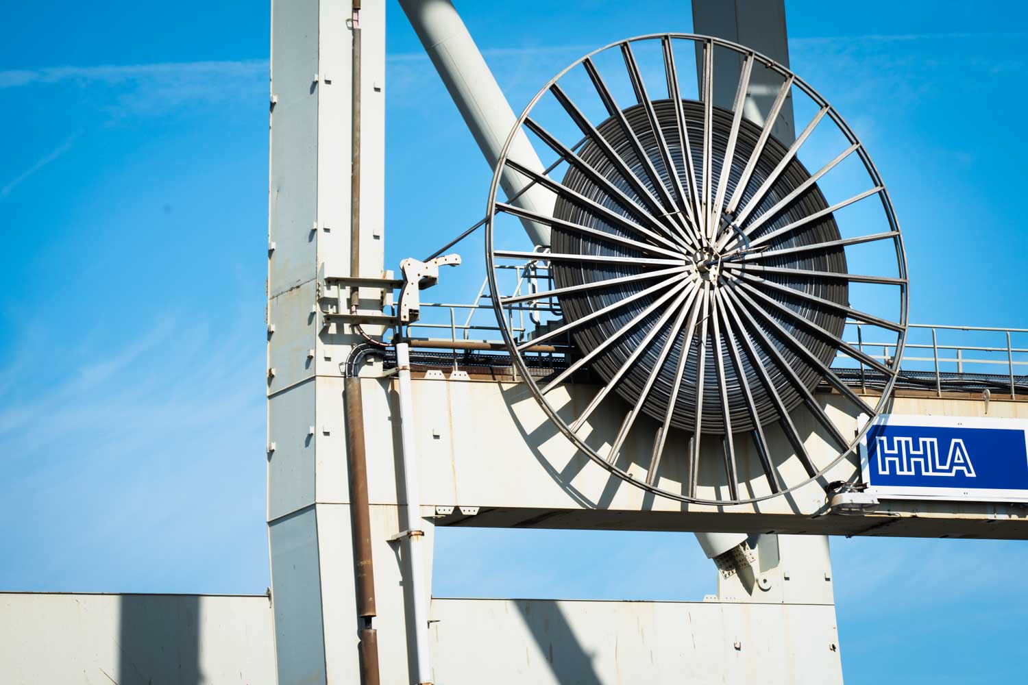 Giant industrial cable reel on a crane against blue sky, labeled with HHLA.