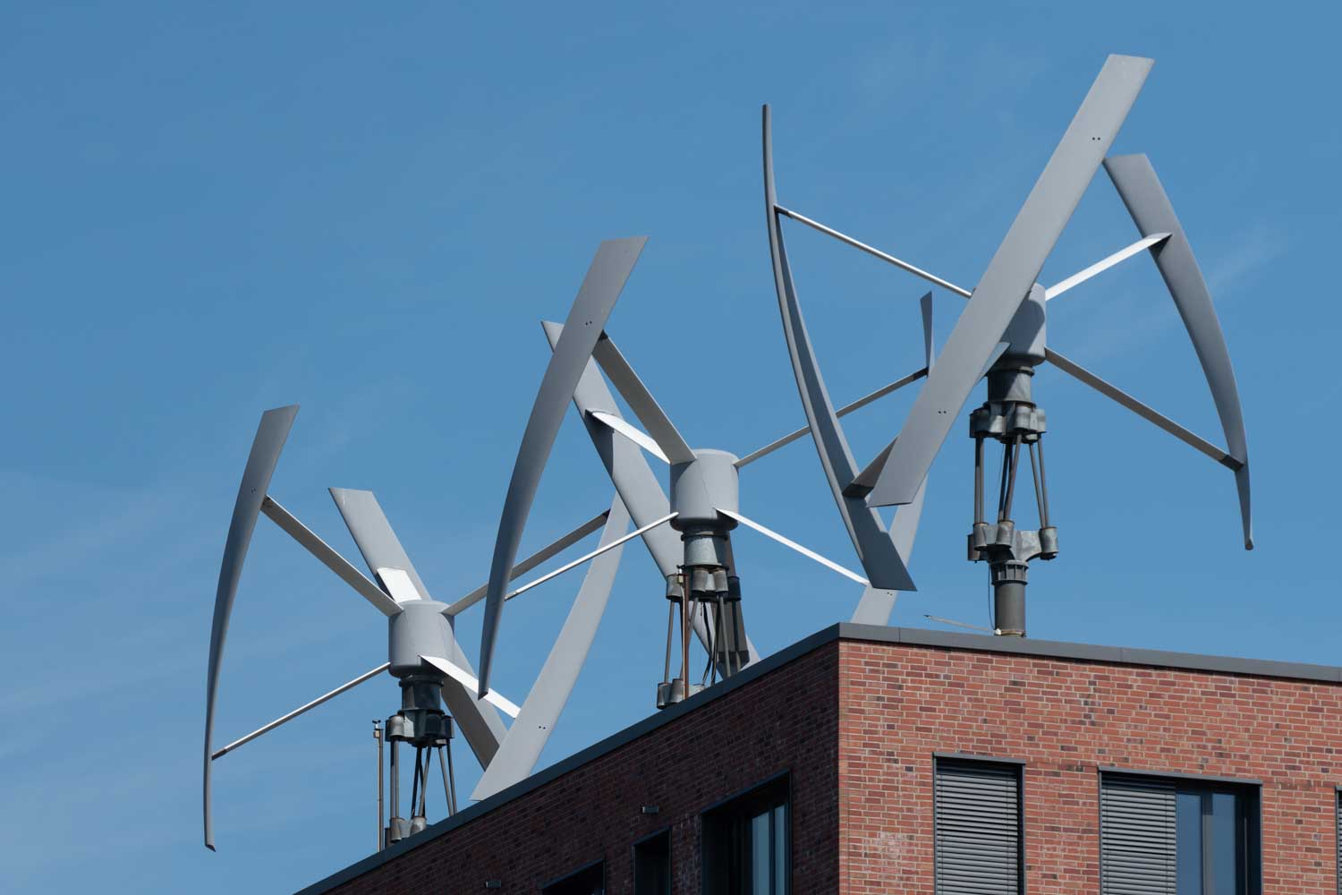 Rooftop vertical wind turbines on a brick building against a clear blue sky.