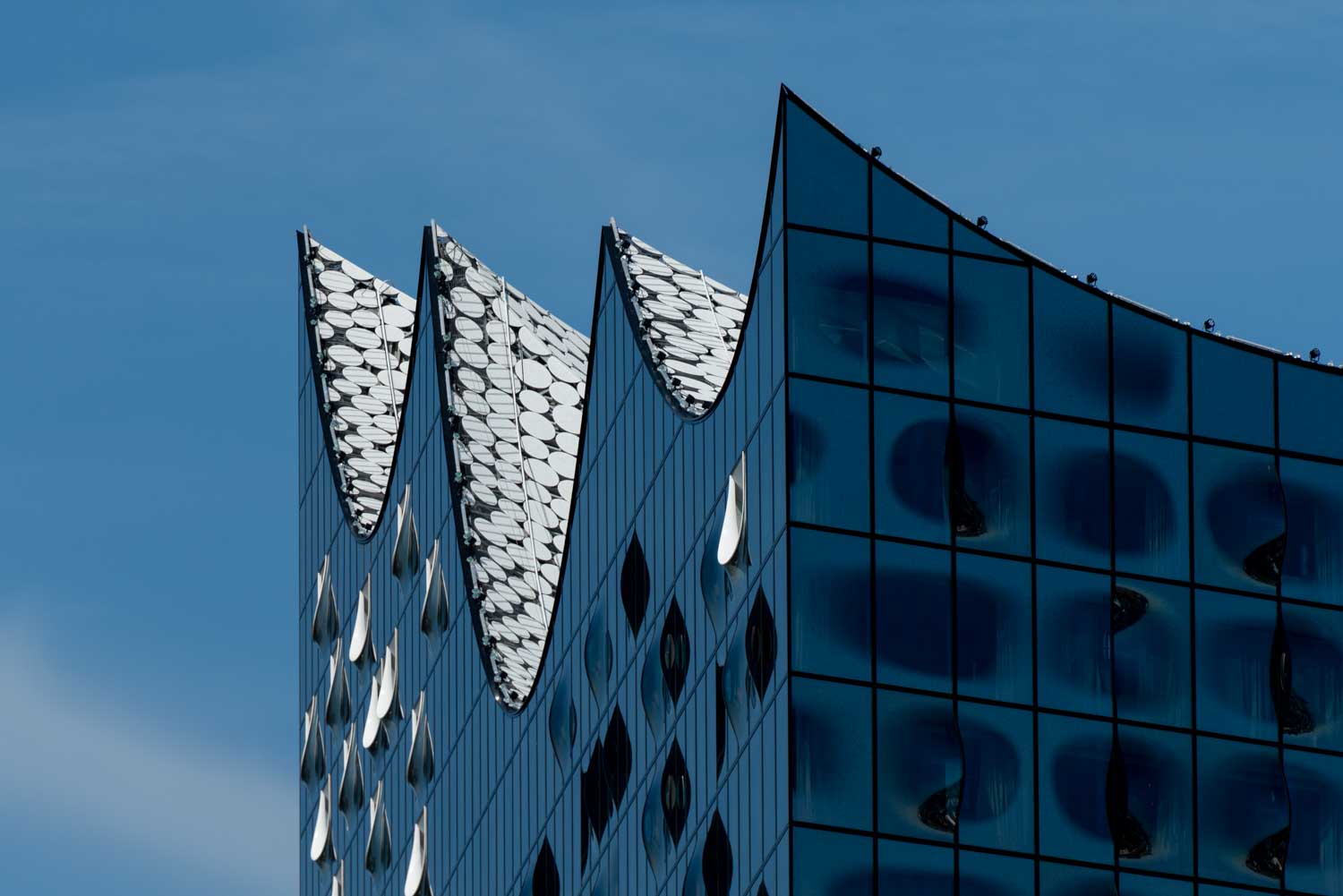 Modern glass building with a wave-like rooftop design against a clear blue sky.