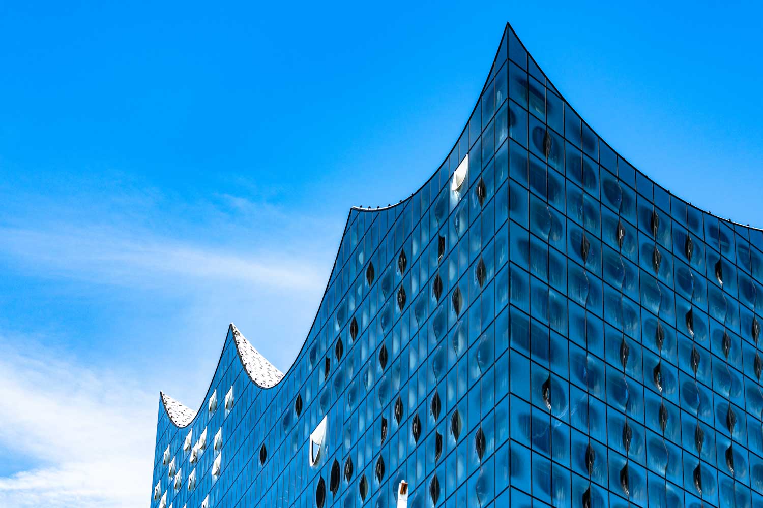 Modern glass building with curved roof against a clear blue sky, detailing reflective windows and sleek design.