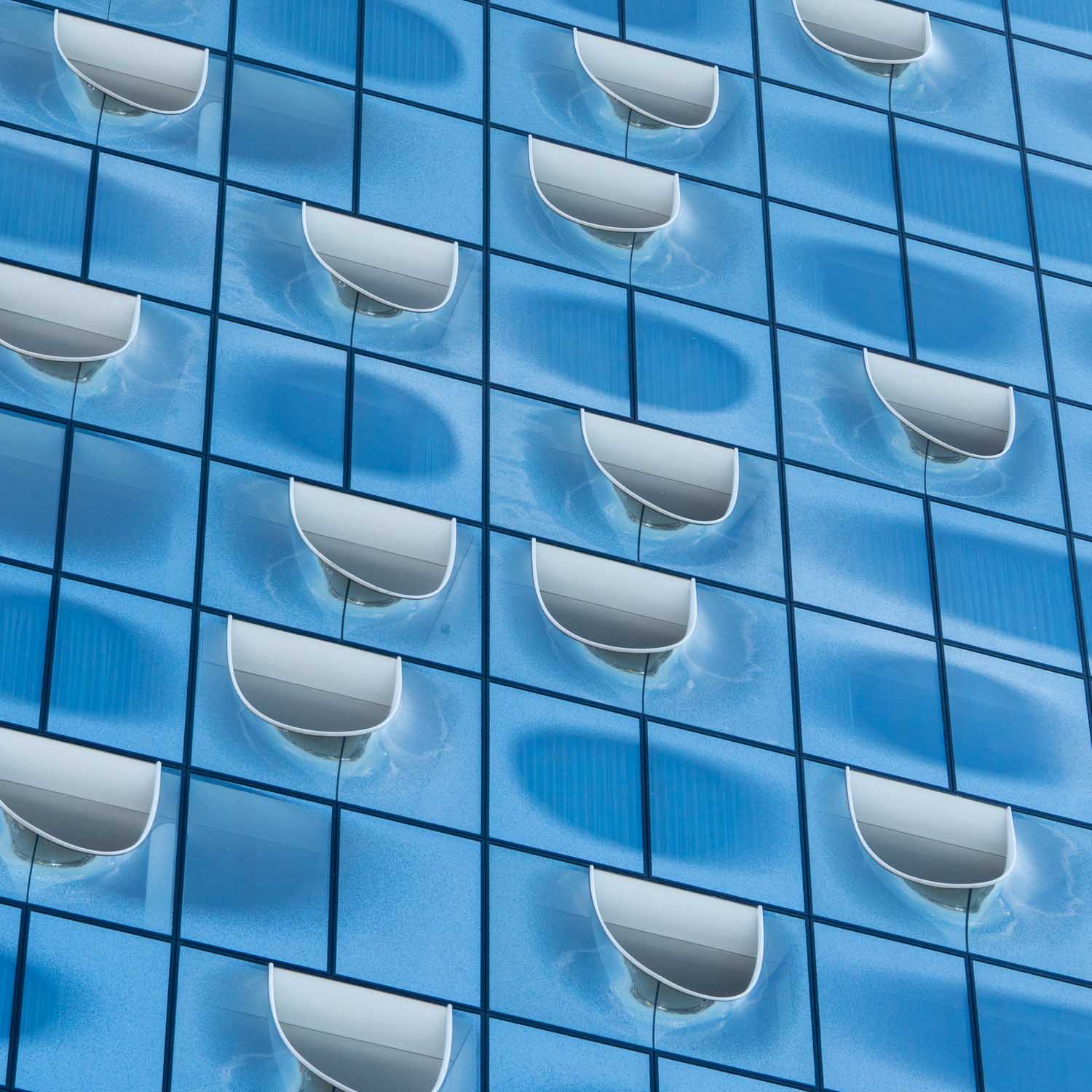 Glass facade with unique curved windows reflecting light, featuring a modern architectural pattern.