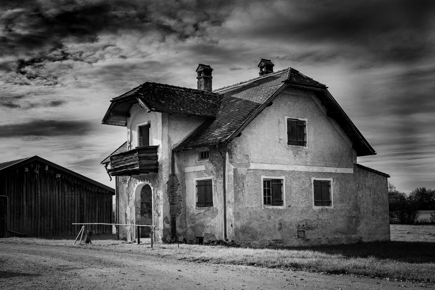 Old rural house with a wooden balcony under a dramatic cloudy sky in black and white.