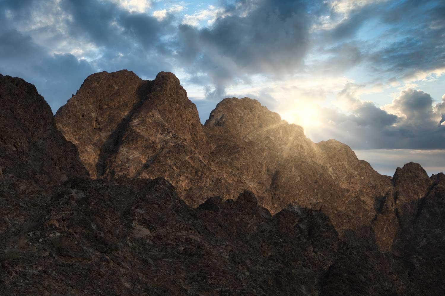 Rocky mountains at sunrise with sunbeams breaking through clouds, creating a dramatic and scenic landscape view.