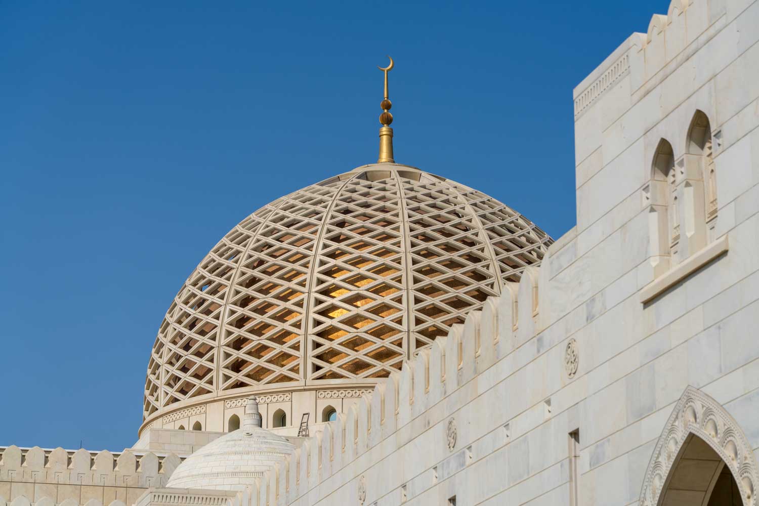 Intricate dome architecture of a mosque under a clear blue sky, showcasing lattice design and crescent finial.