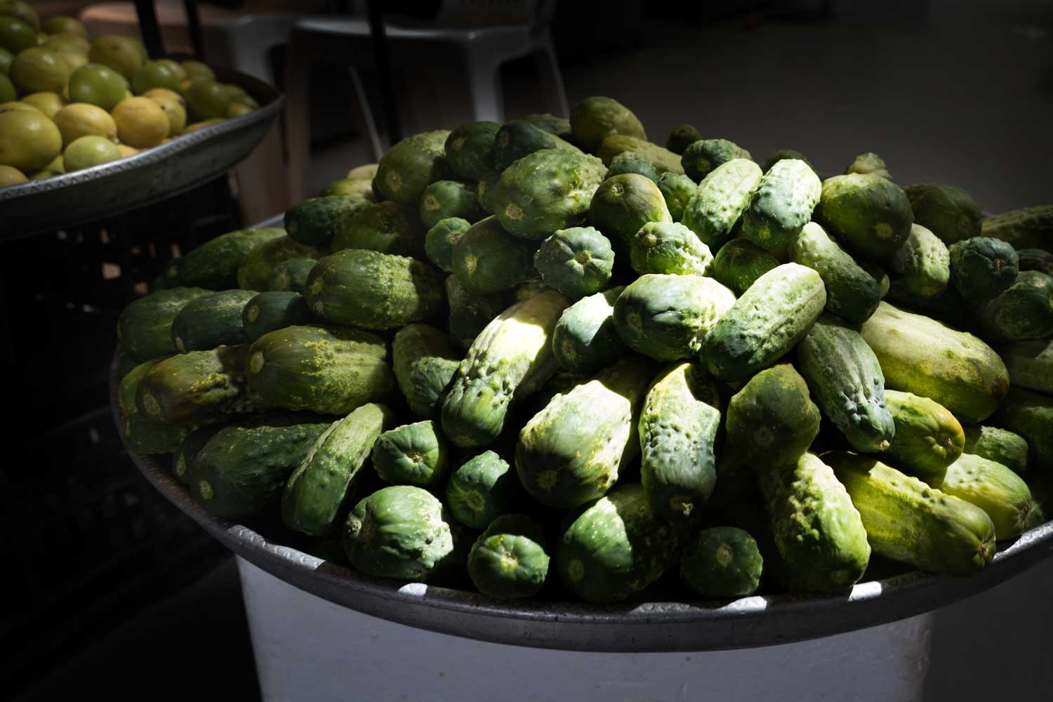 Pile of fresh green cucumbers on display at a market stall with sunlight highlighting their texture.