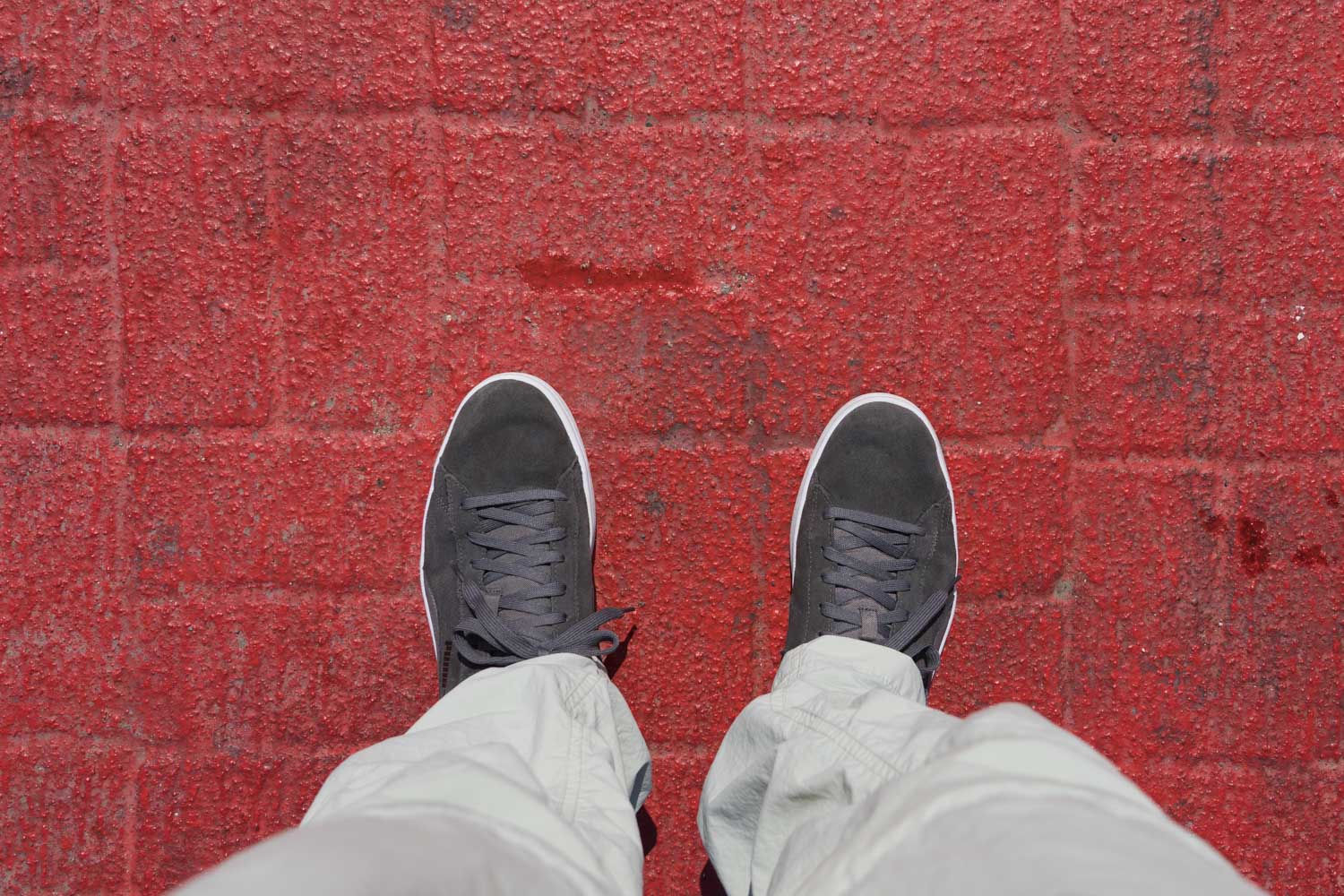 Person wearing gray sneakers and light pants standing on a red textured brick pavement.