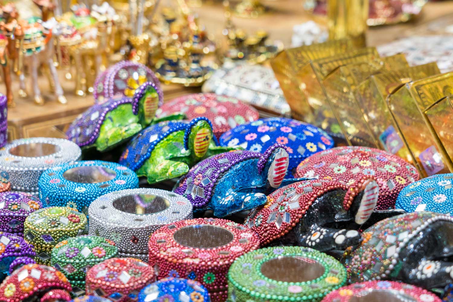 Colorful, beaded decorative boxes and vibrant animal figurines displayed on a market stall table.