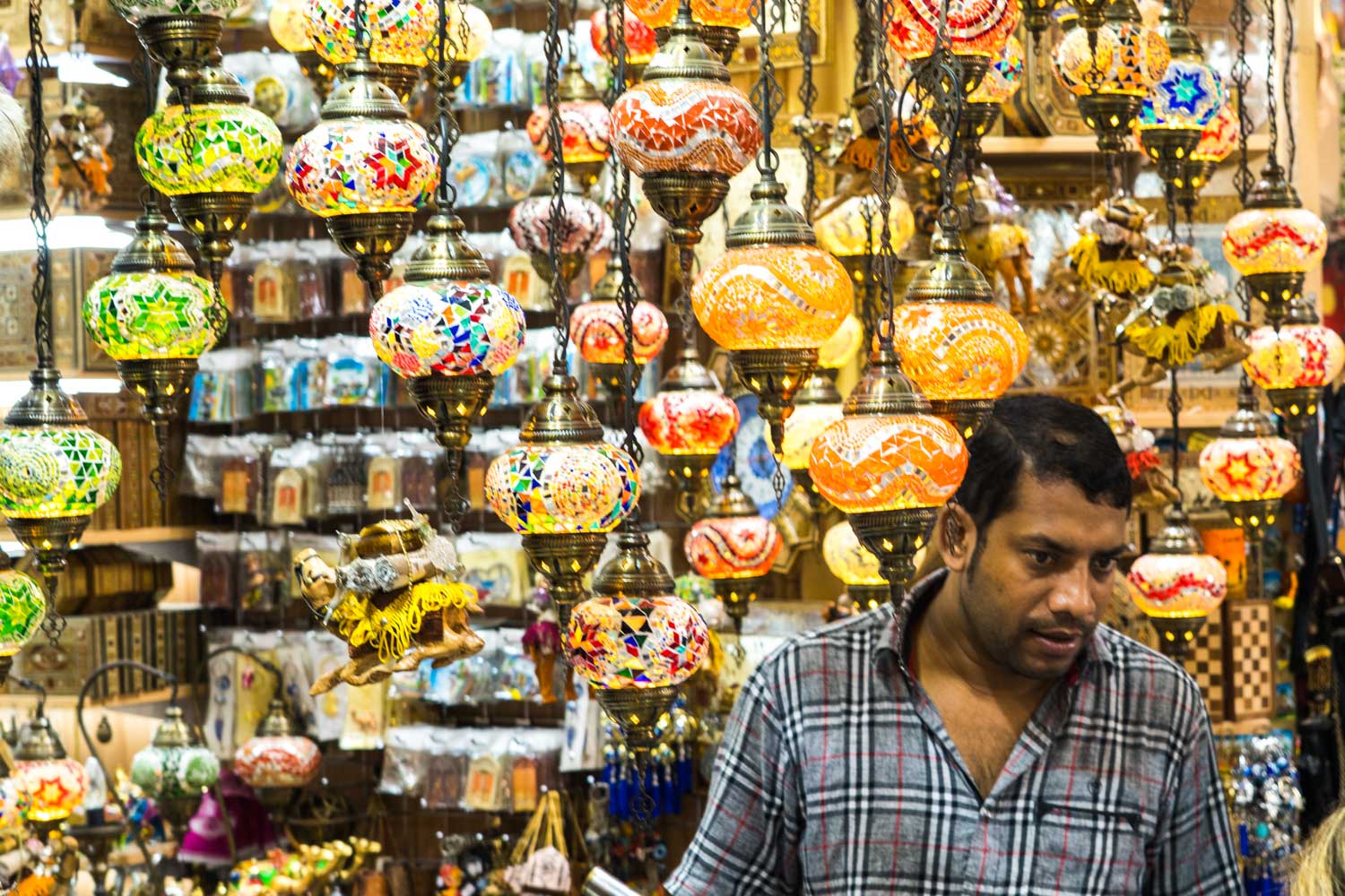 A shopkeeper stands amid colorful Turkish mosaic lamps in a vibrant bazaar.