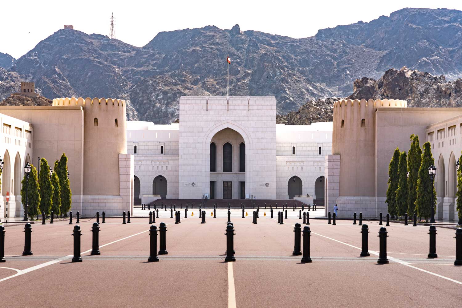 Grand palace entrance with arched windows, set against rocky mountains under a clear sky.