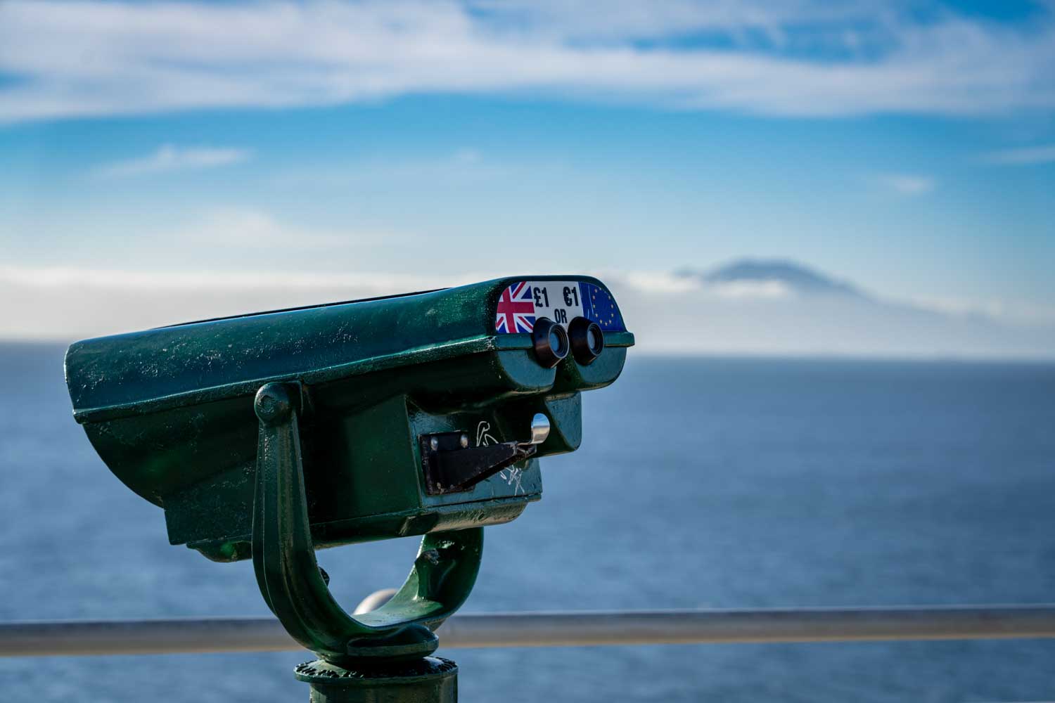Coin-operated binoculars facing the ocean with a distant mountain view under a blue sky.
