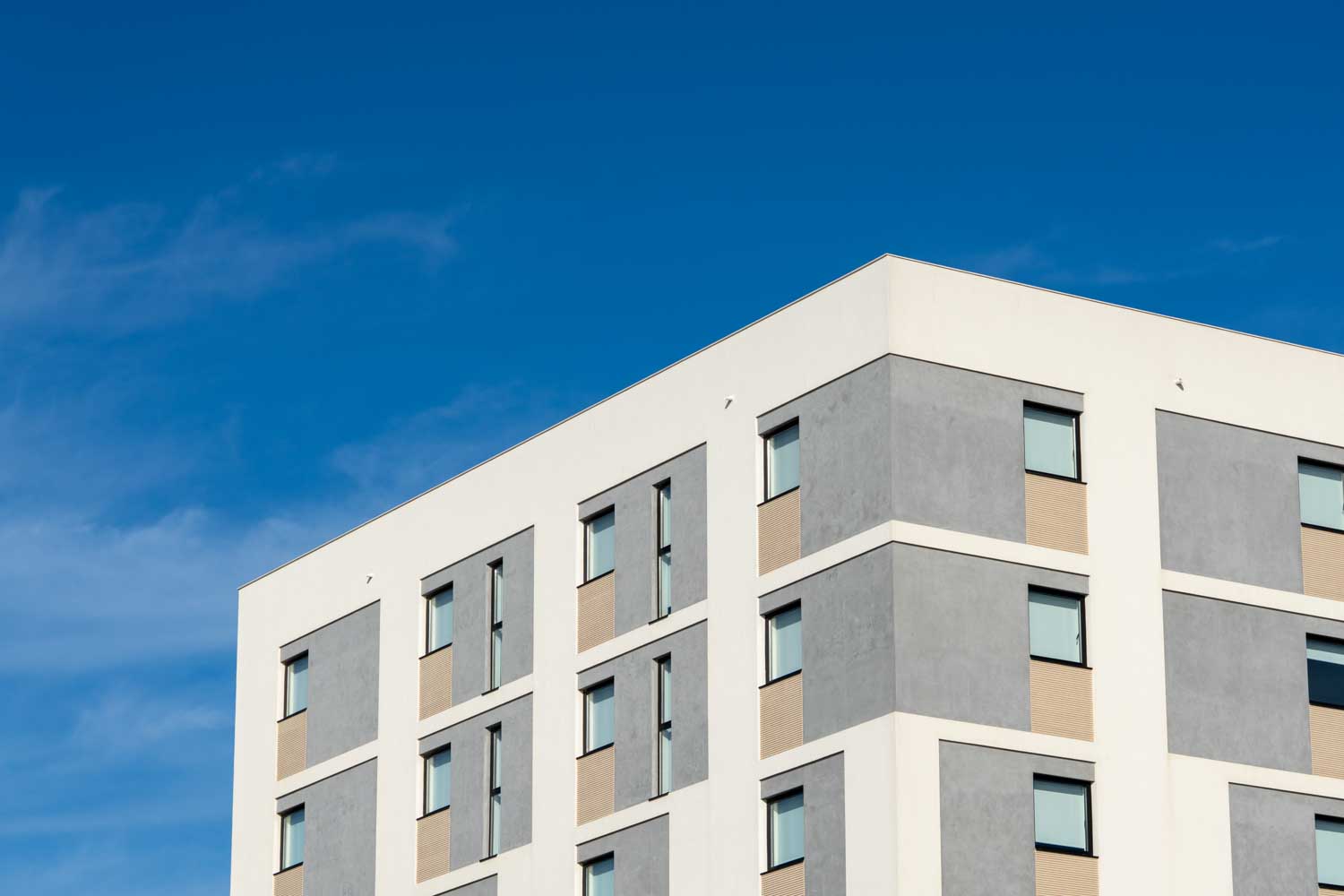 Modern building with gray and white facade against a clear blue sky.