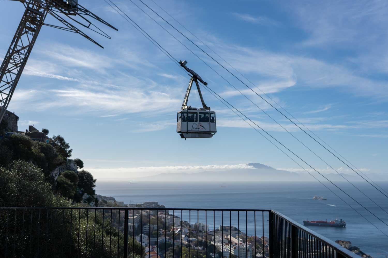 Cable car suspended over a coastal city with ocean and mountain views in the distance on a clear, sunny day.