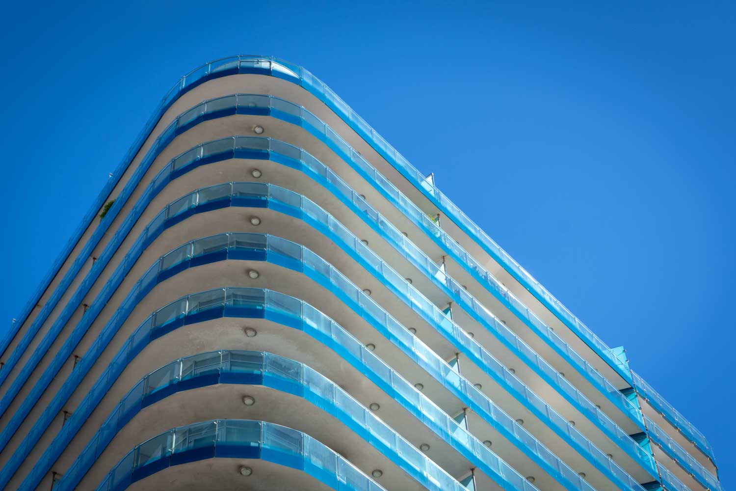 Modern building with rounded balconies and glass railings against a clear blue sky.