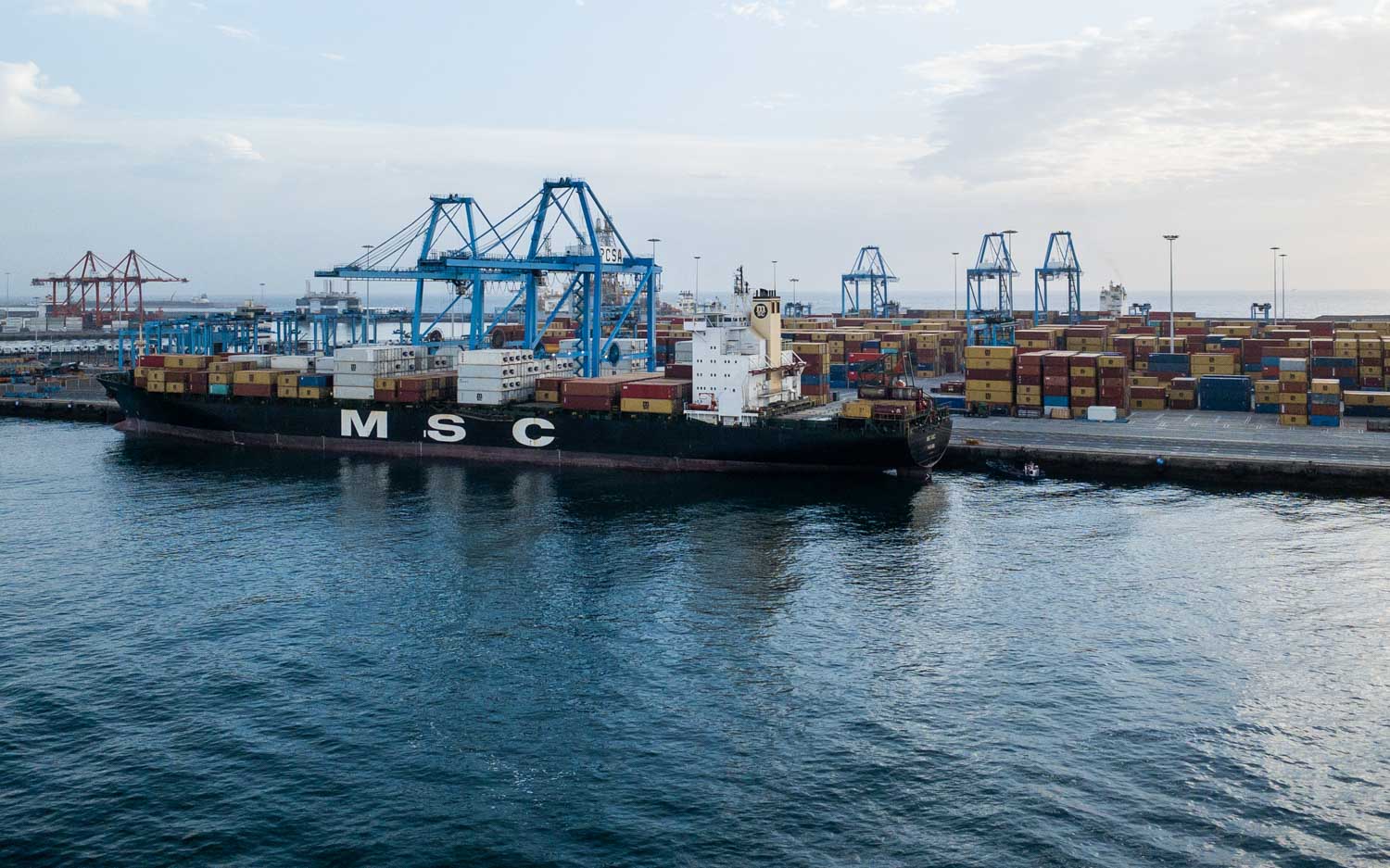 Cargo ship at busy port with stacked containers and cranes on a clear day.