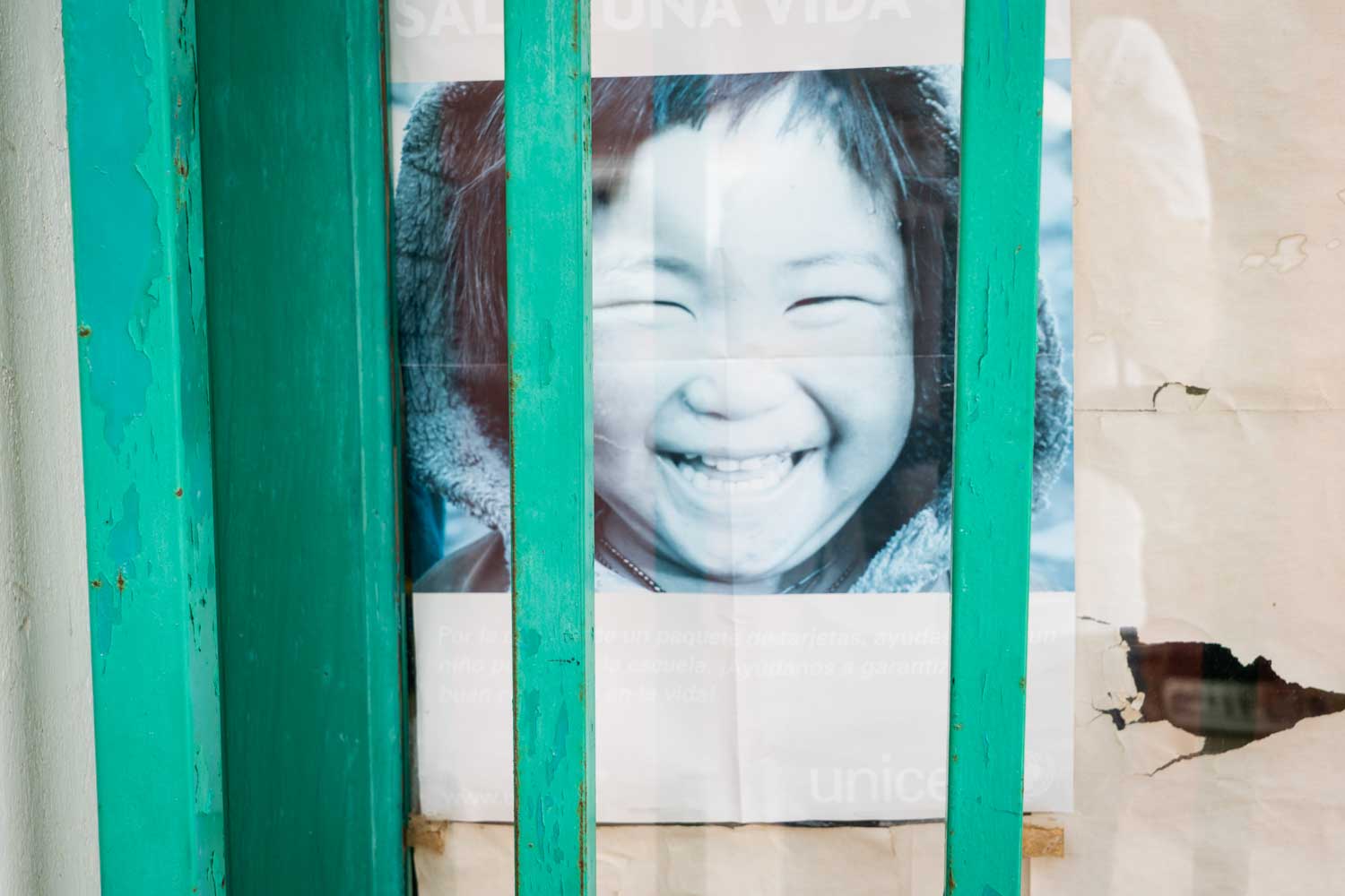 Smiling child on UNICEF poster behind green wooden window frame.