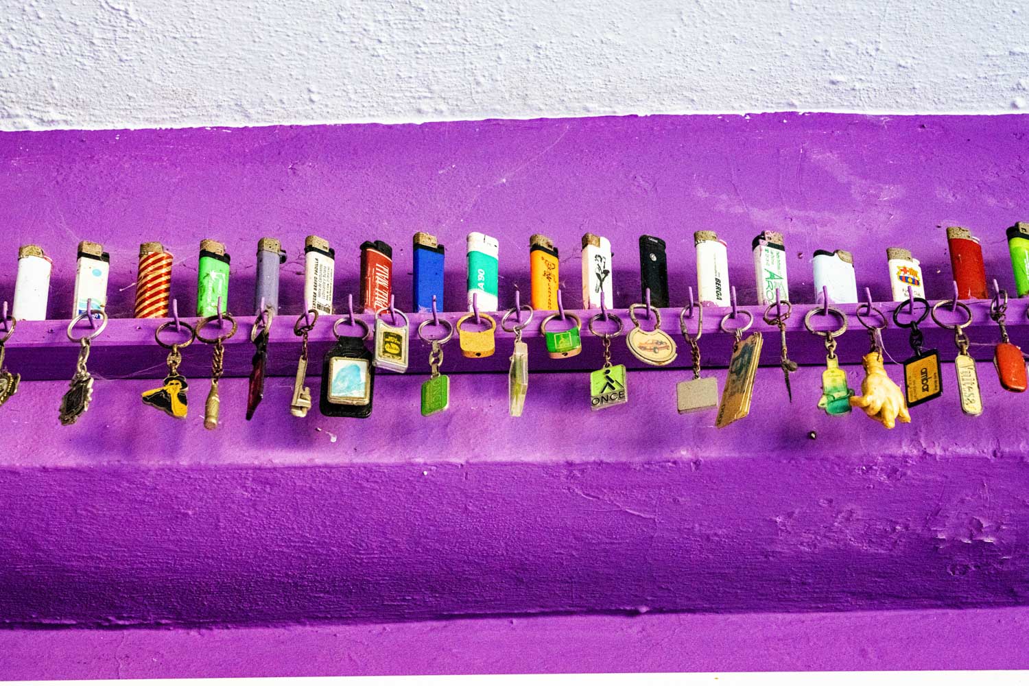 Colorful lighters with keychains on a purple rack against a white wall.