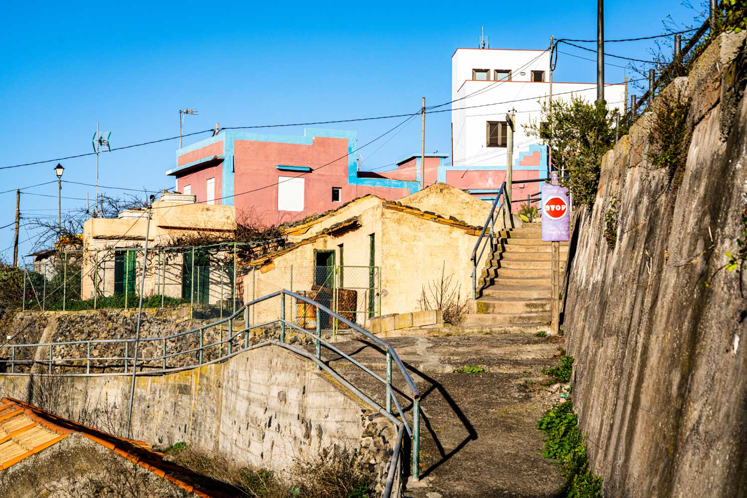 Colorful hillside houses with a stairway, blue sky, and a STOP sign in a scenic Mediterranean village.