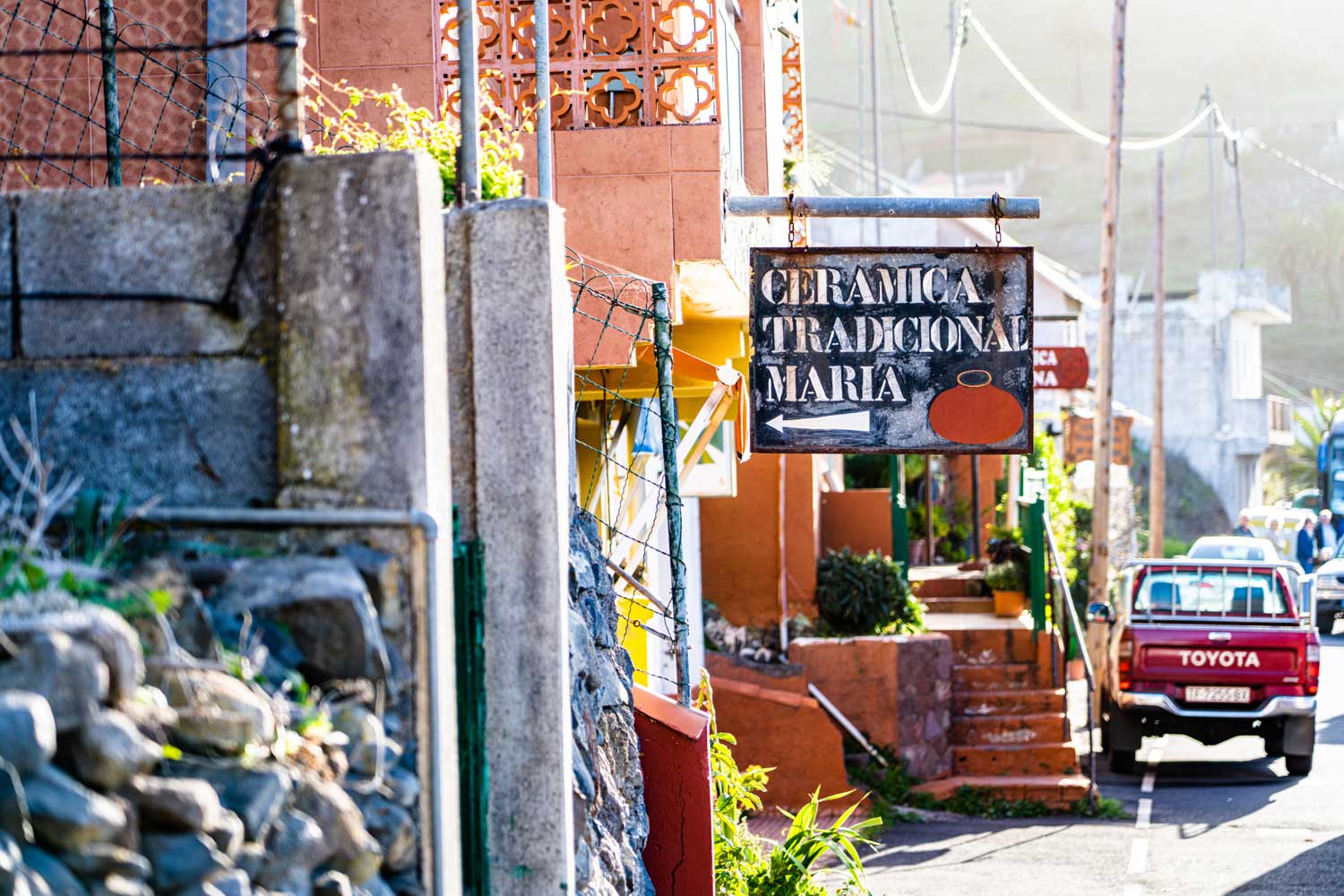 Sign for Ceramica Tradicional Maria on rustic street, beside red Toyota truck and stone wall.
