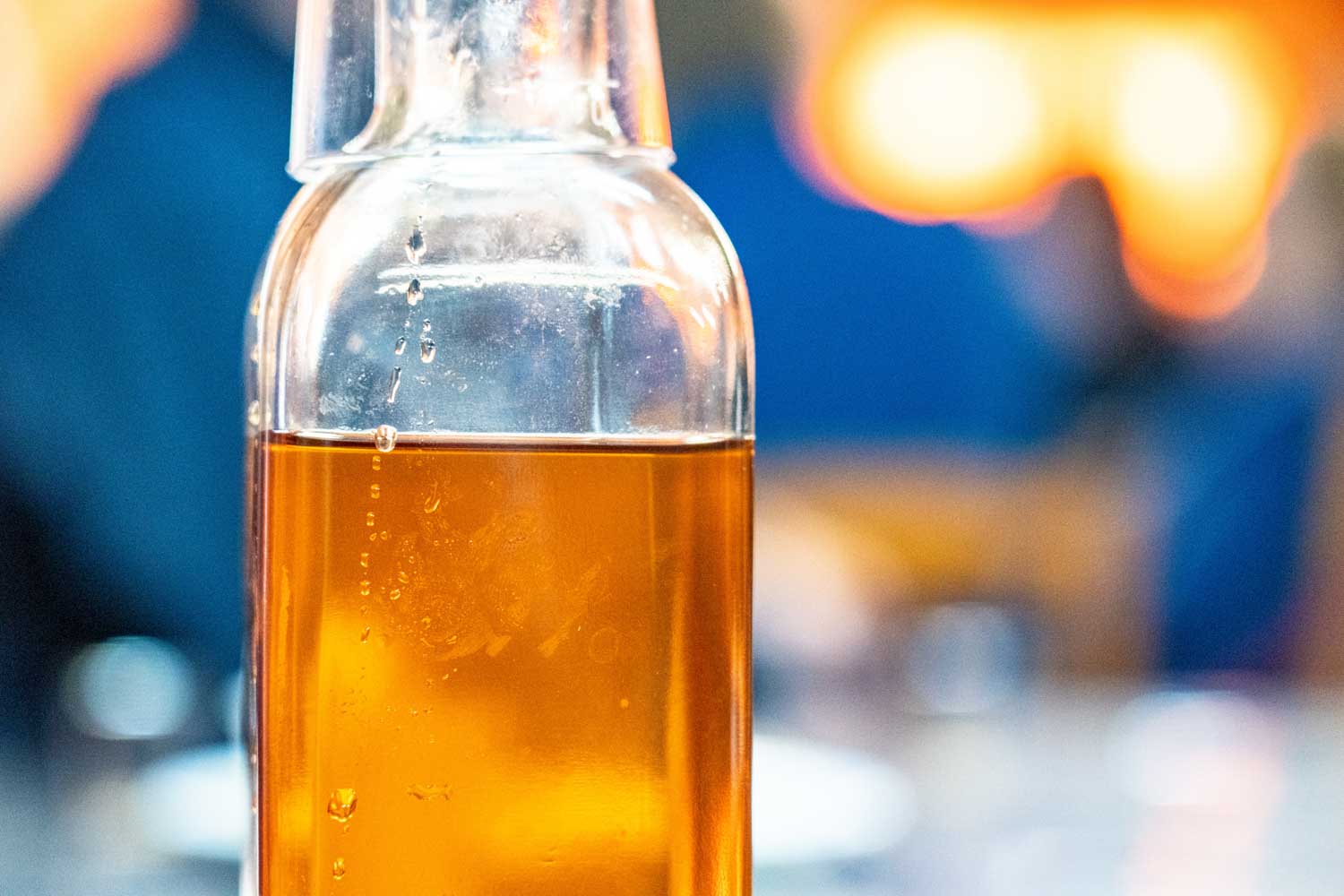 Clear glass bottle filled with amber liquid against a blurred background with warm lights.