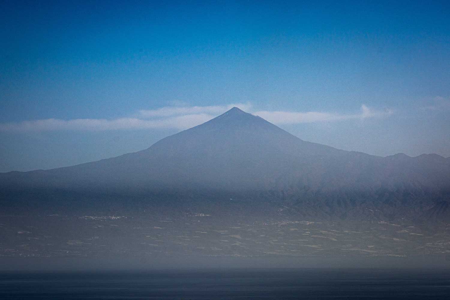 Distant view of a mountain peak under a clear blue sky, with a hazy landscape below.