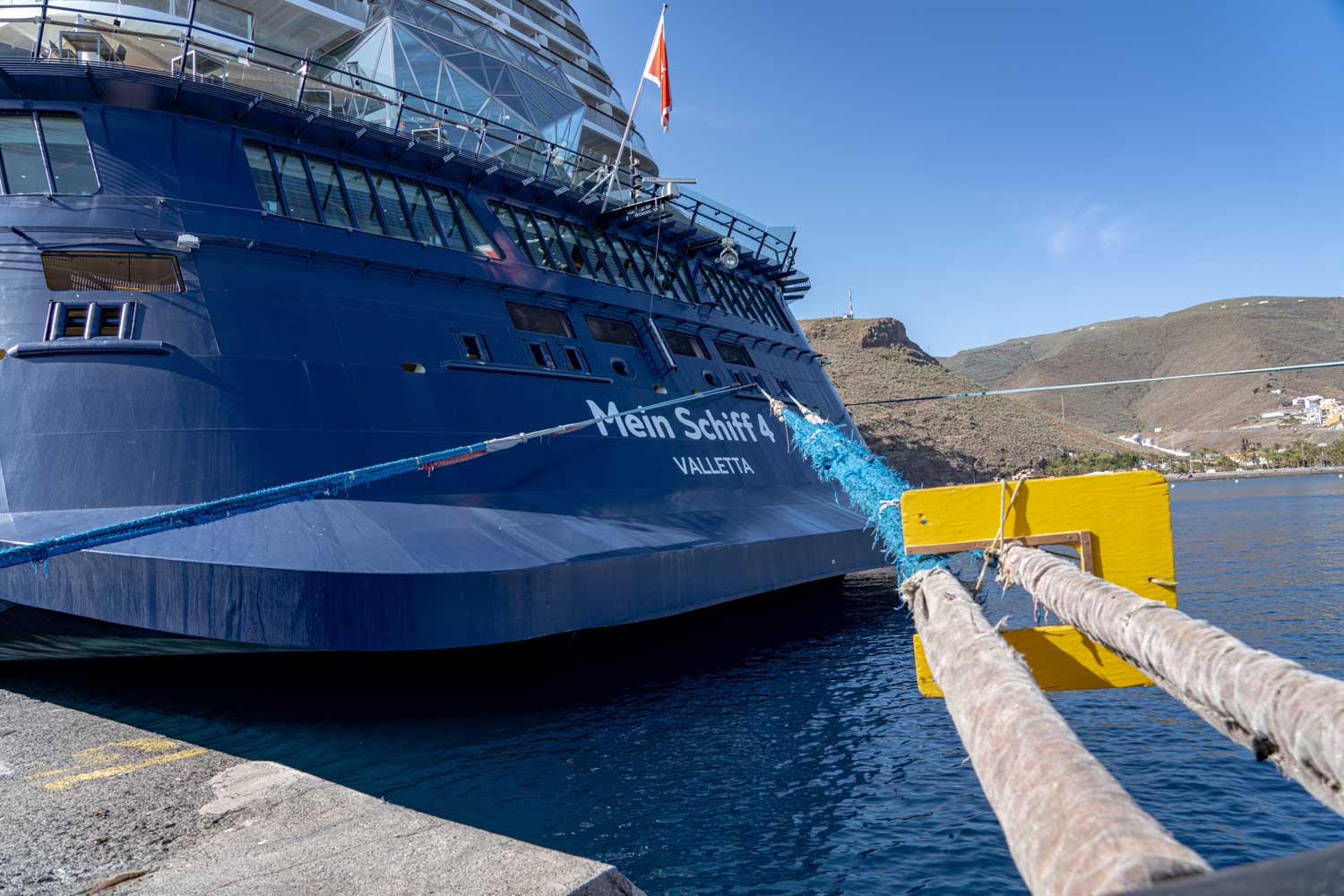 Cruise ship Mein Schiff 4 docked at picturesque port with clear blue skies and distant hills.