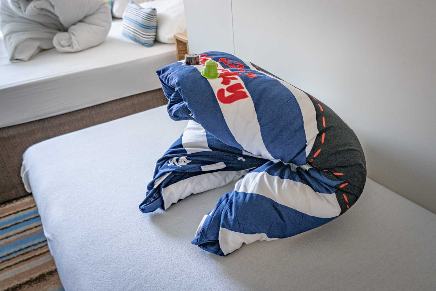 A neatly folded blue-and-white striped blanket on a bed with toy figures on top, next to a decorative pillow.