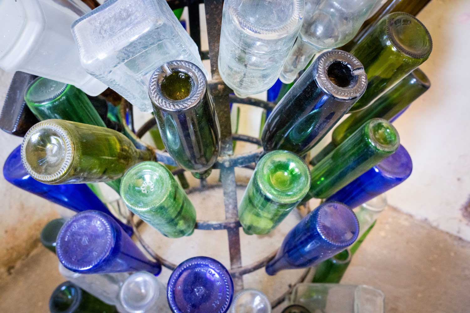 Colorful glass bottles arranged upside down on a drying rack, featuring green, blue, and clear bottles.
