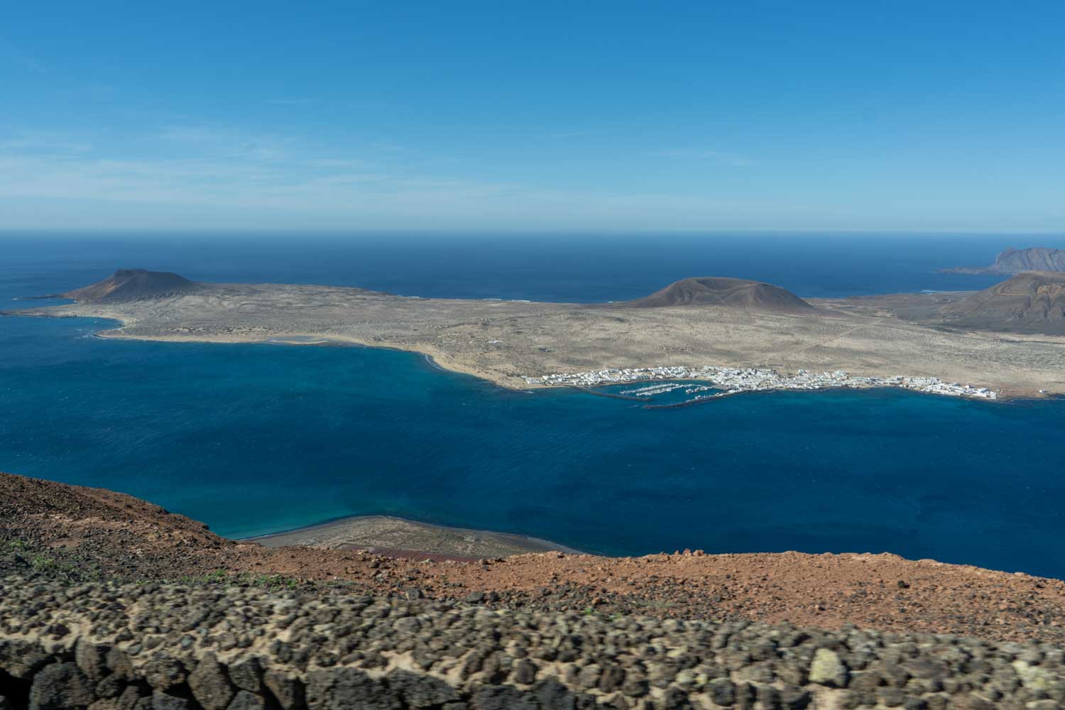 Aerial view of La Graciosa island with volcanic landscapes and blue ocean under a clear sky in Canary Islands.