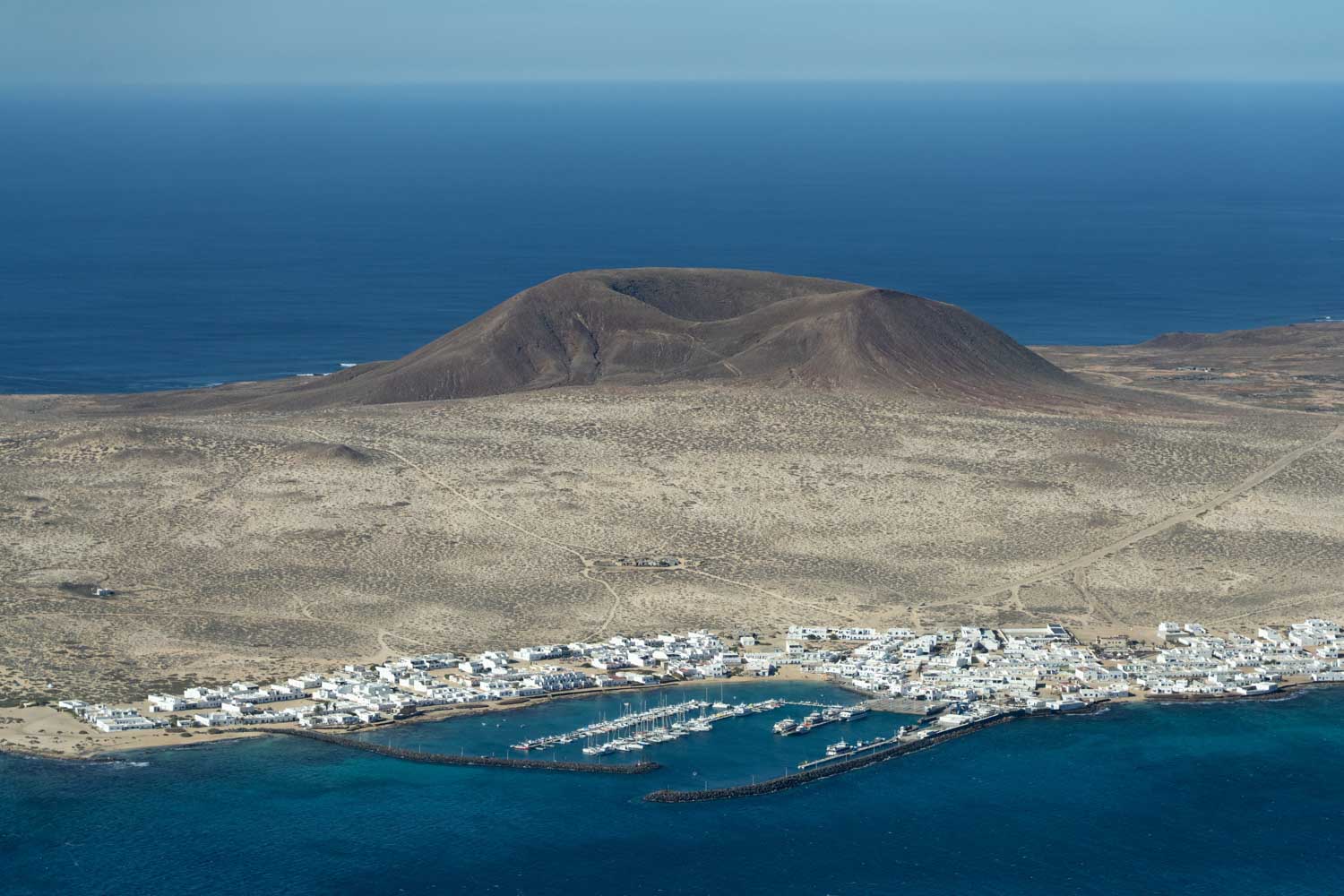 Aerial view of Lanzarote island coastline with a volcanic crater and a whitewashed village by the blue ocean, Spain.