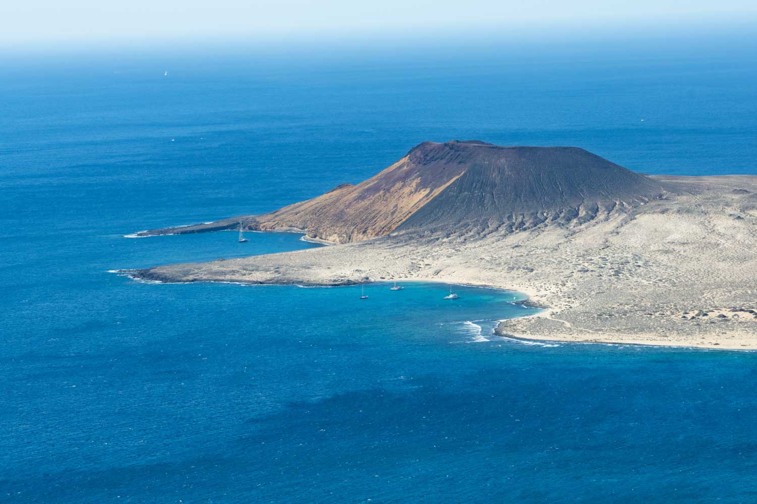 Aerial view of La Graciosa Island's barren volcanic landscape surrounded by vibrant blue ocean waters.