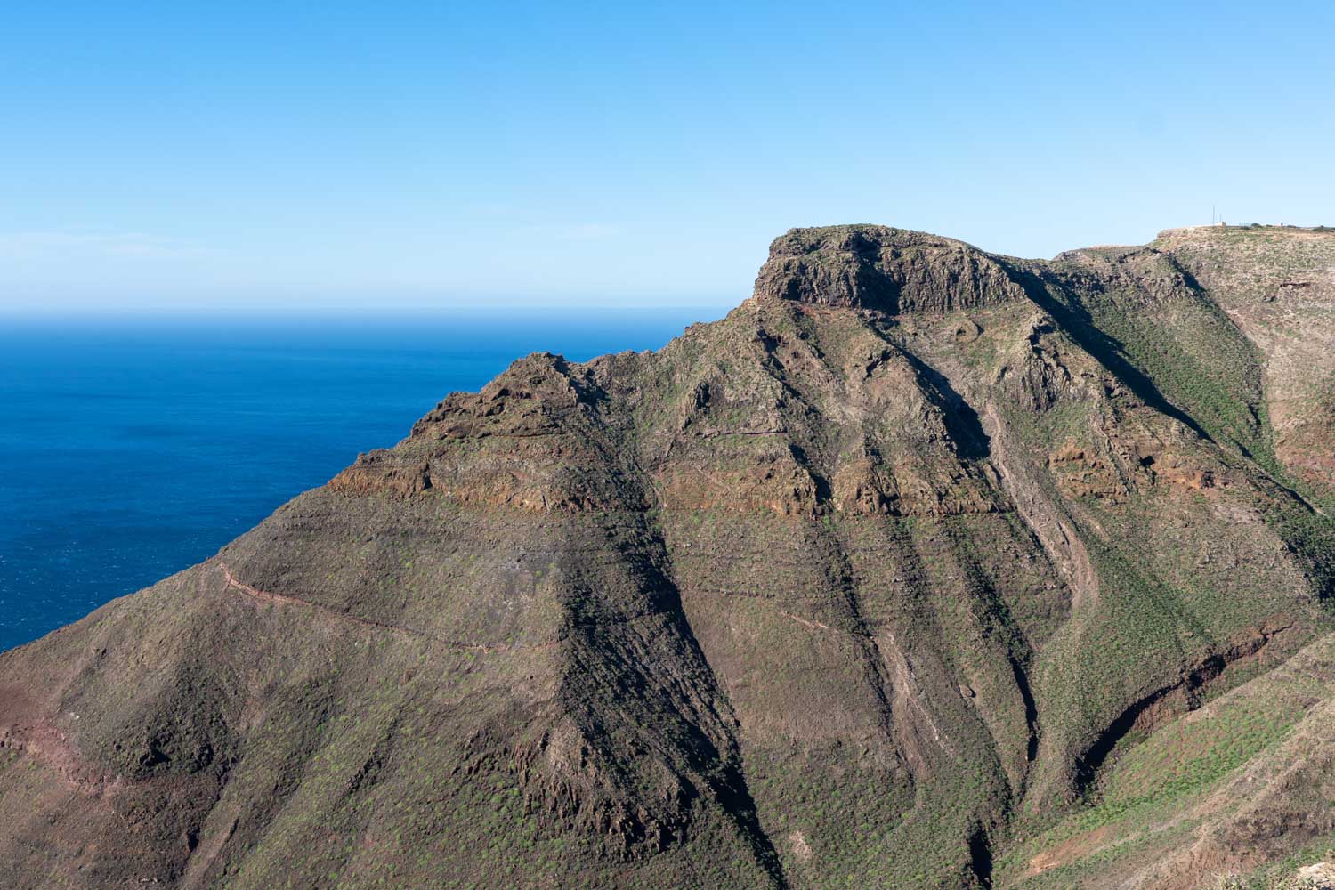 Rugged mountain landscape with cliff faces and ocean view under clear blue sky.