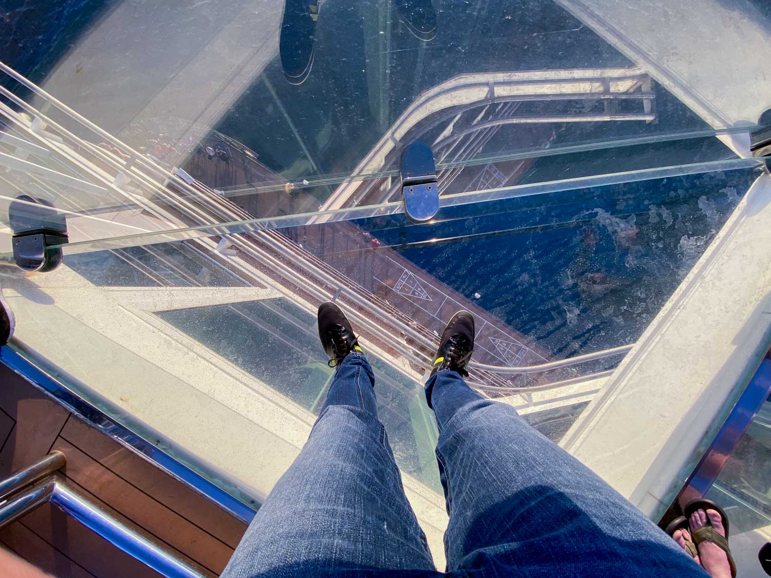 View of feet standing on a glass walkway with a cityscape below.