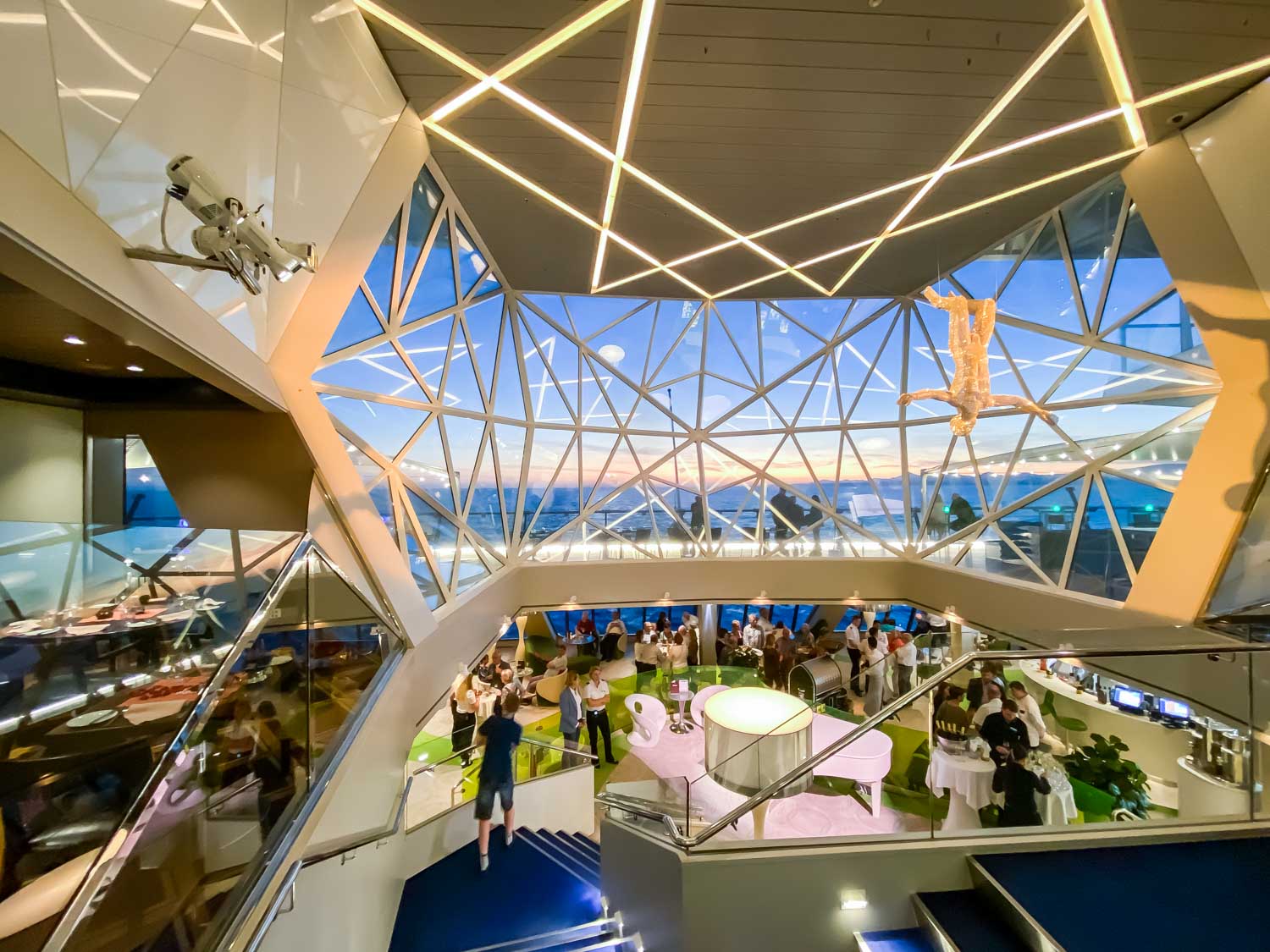 Futuristic dining area with geometric windows, modern decor, and a crowd of people at a social event.