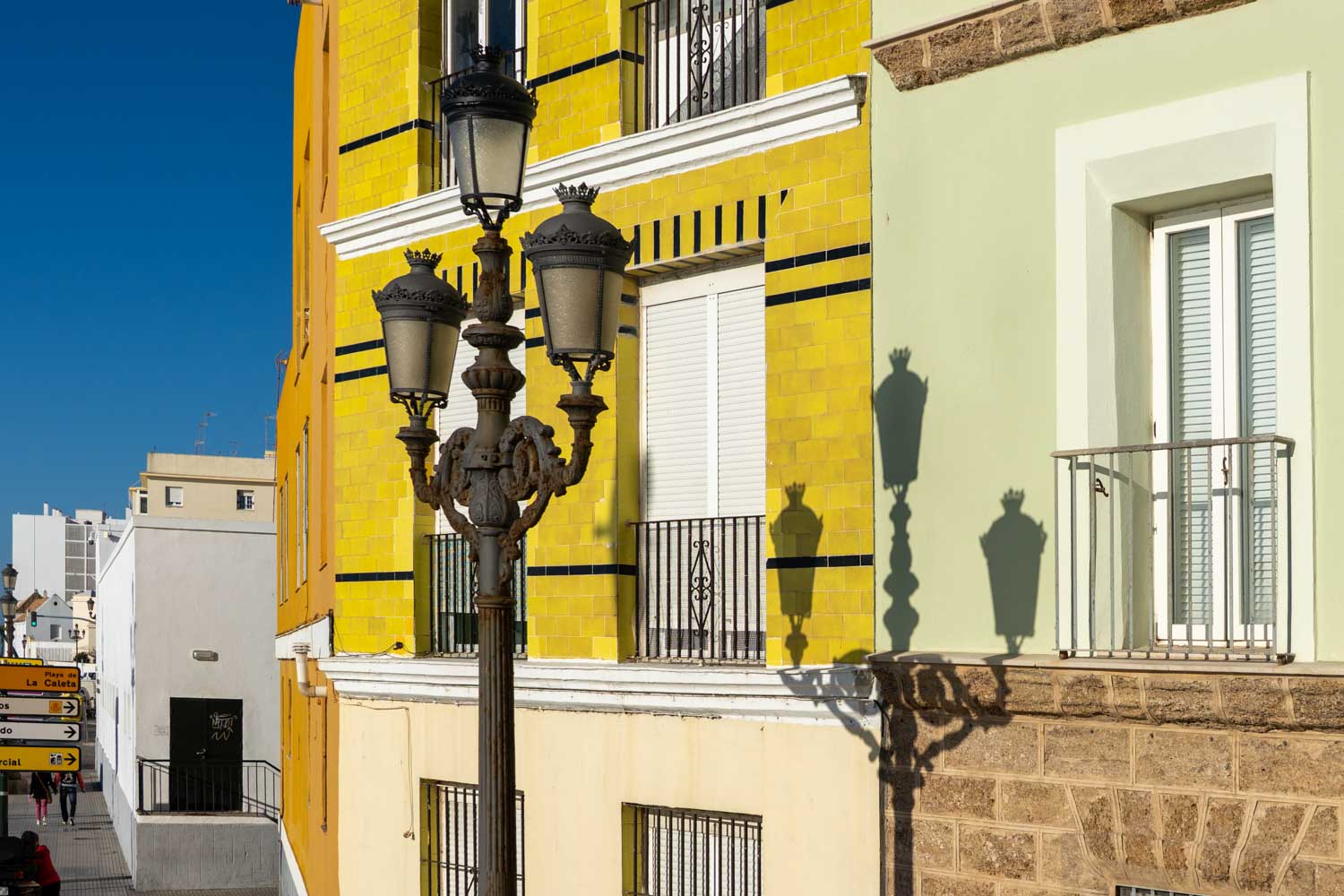 Historic street lamp casting shadow on bright yellow building with balconies under clear blue sky.