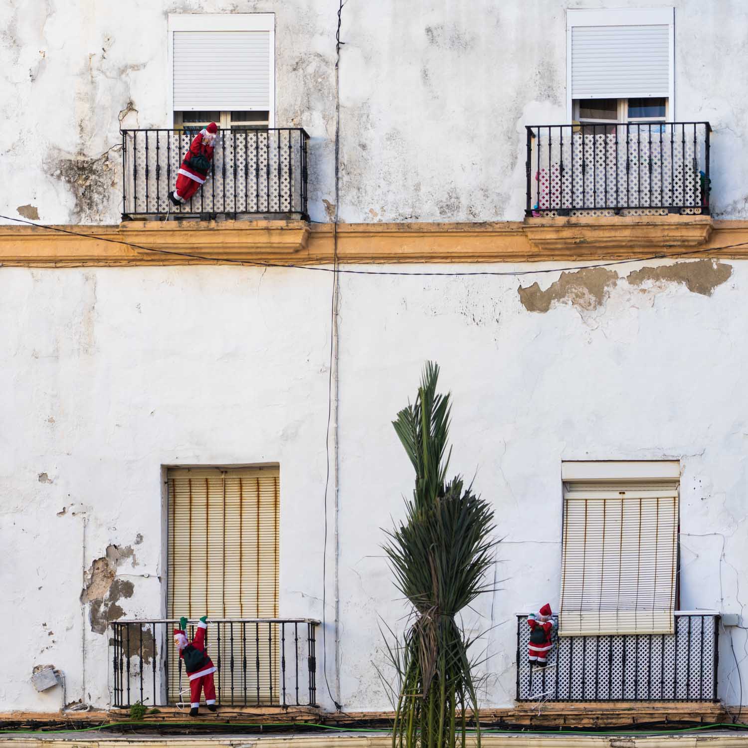 Santa Claus dolls climbing balconies of a weathered building, adding festive cheer to the urban scene.