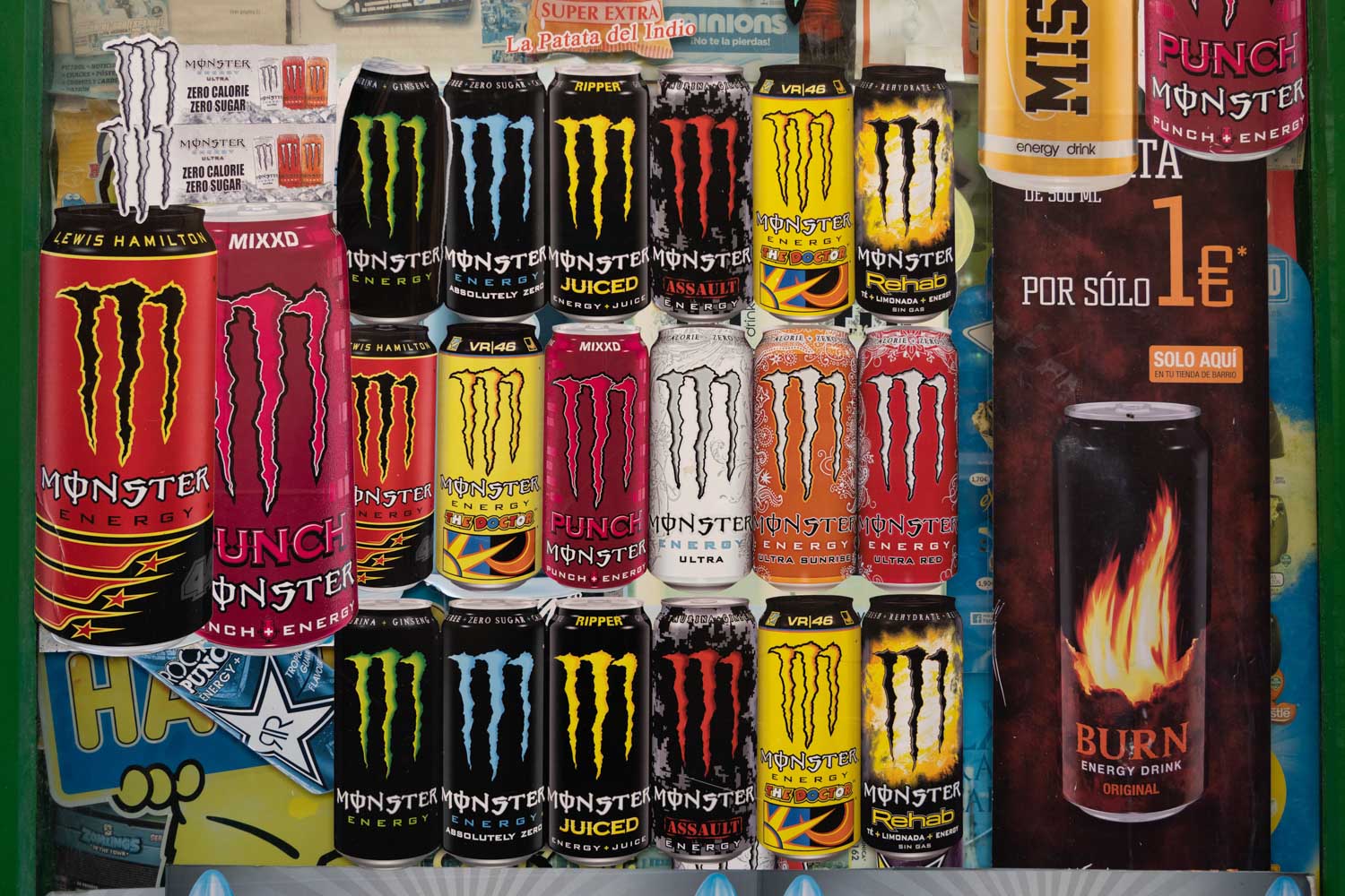 Assorted Monster and Burn energy drink cans displayed on a colorful shelf backdrop.