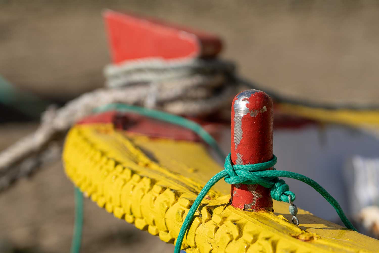 Close-up of a colorful boat detail with red and yellow paint, and a green rope tied around a post.