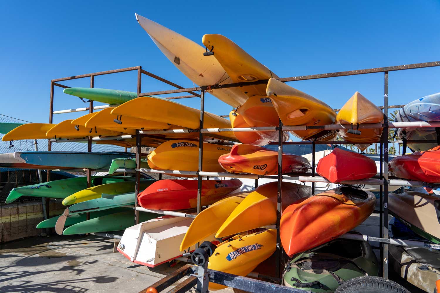 Colorful kayaks stacked on a metal rack under a clear blue sky, ready for outdoor adventure.