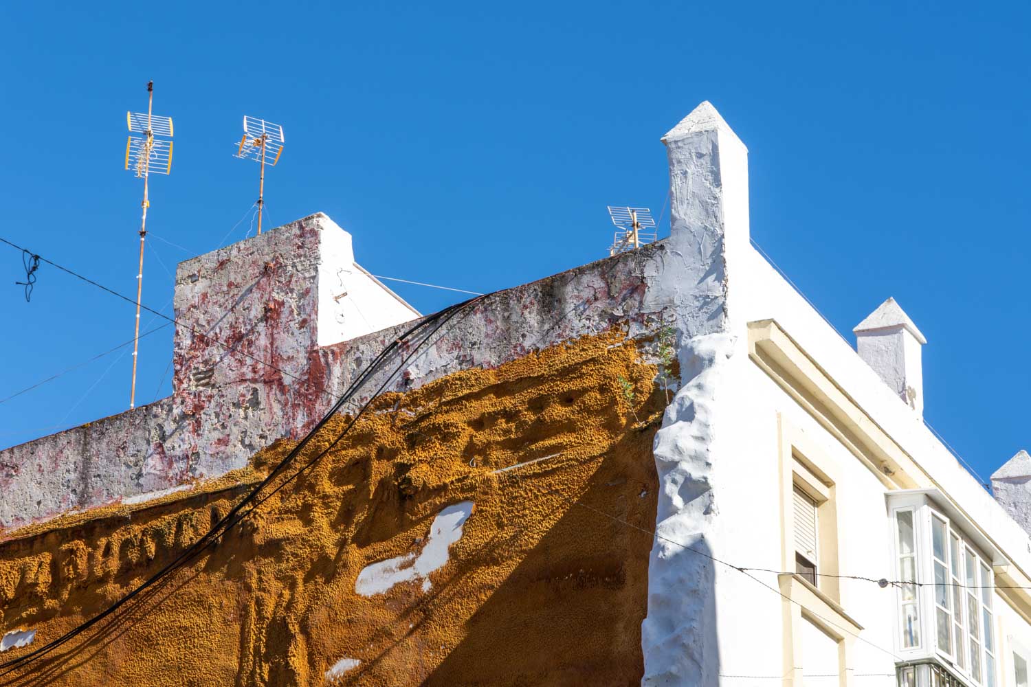 Weathered building facade with orange texture, white accents, and rooftop antennas under a clear blue sky.