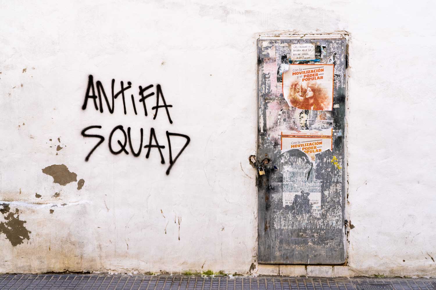 Graffiti reading Antifa Squad on a wall beside a weathered door with torn posters.