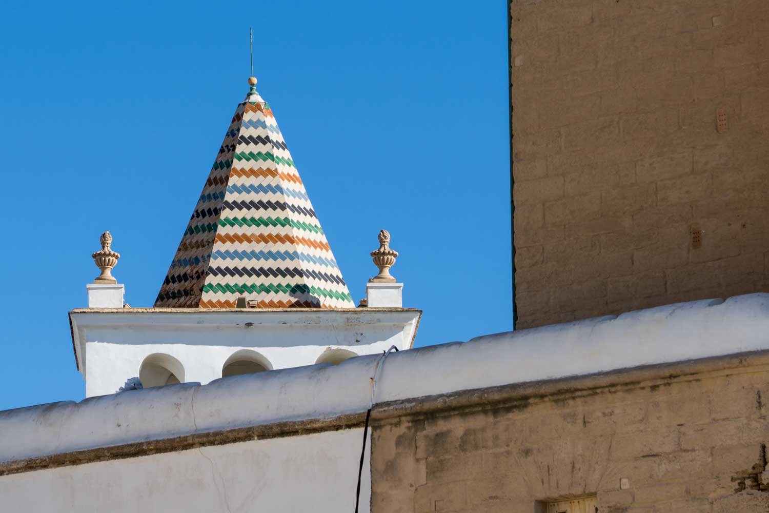 Colorful tiled cone atop historic building under clear blue sky.