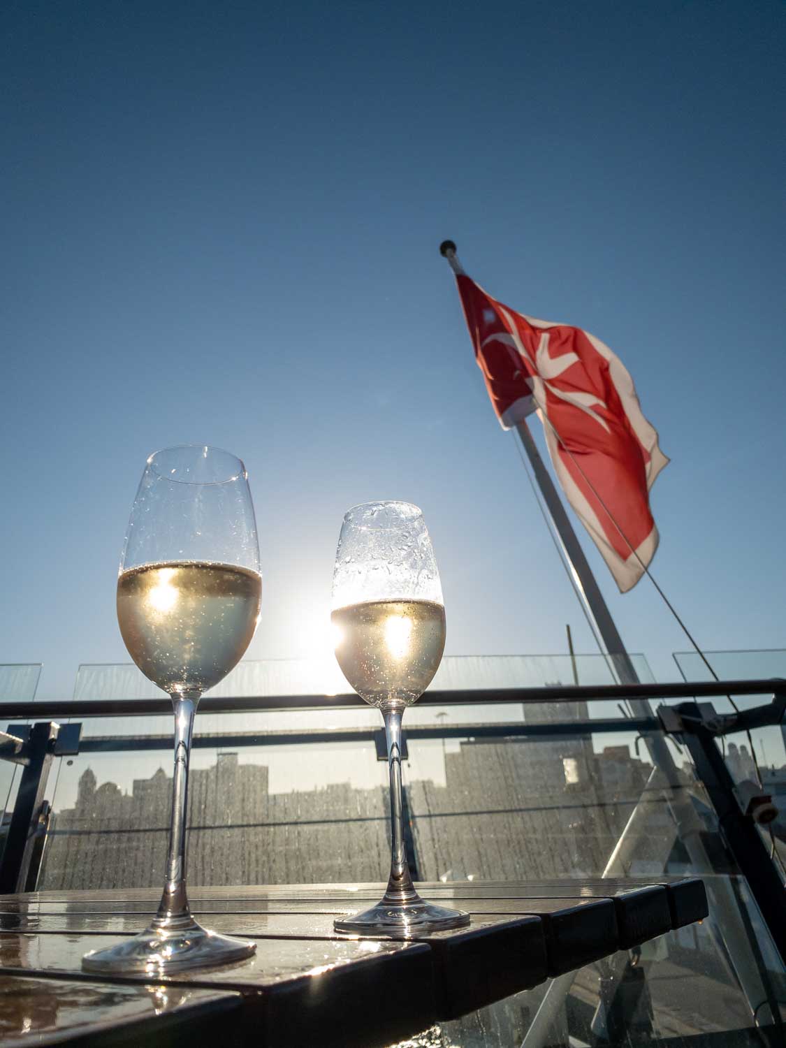 Two glasses of champagne on a sunny rooftop, with a red flag waving in the background.