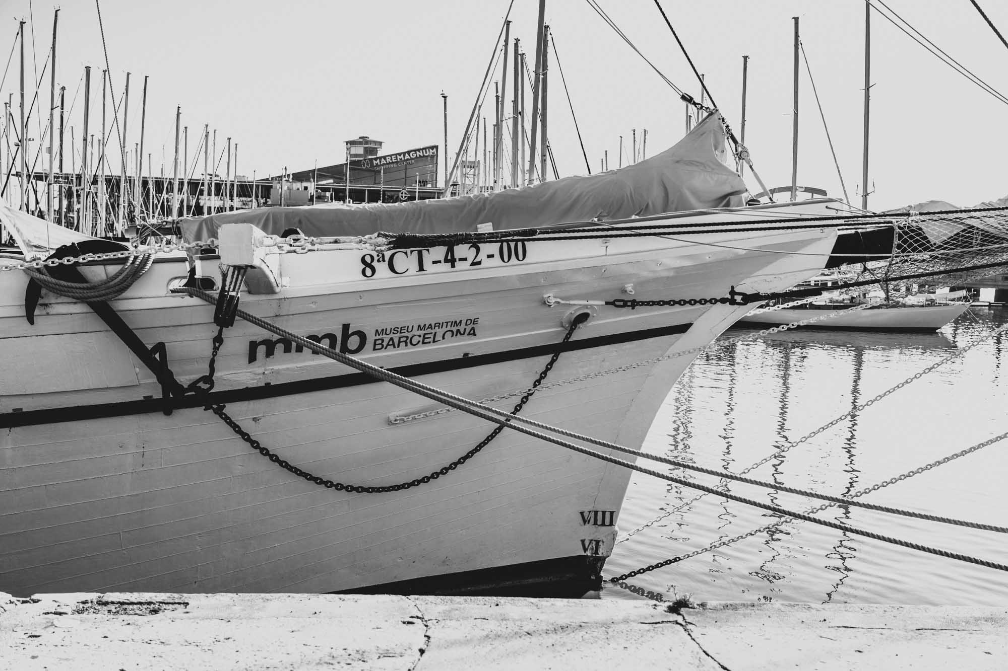 Historic sailboat docked at the Maritime Museum in Barcelona, with masts reflecting on the water. Black and white photo.