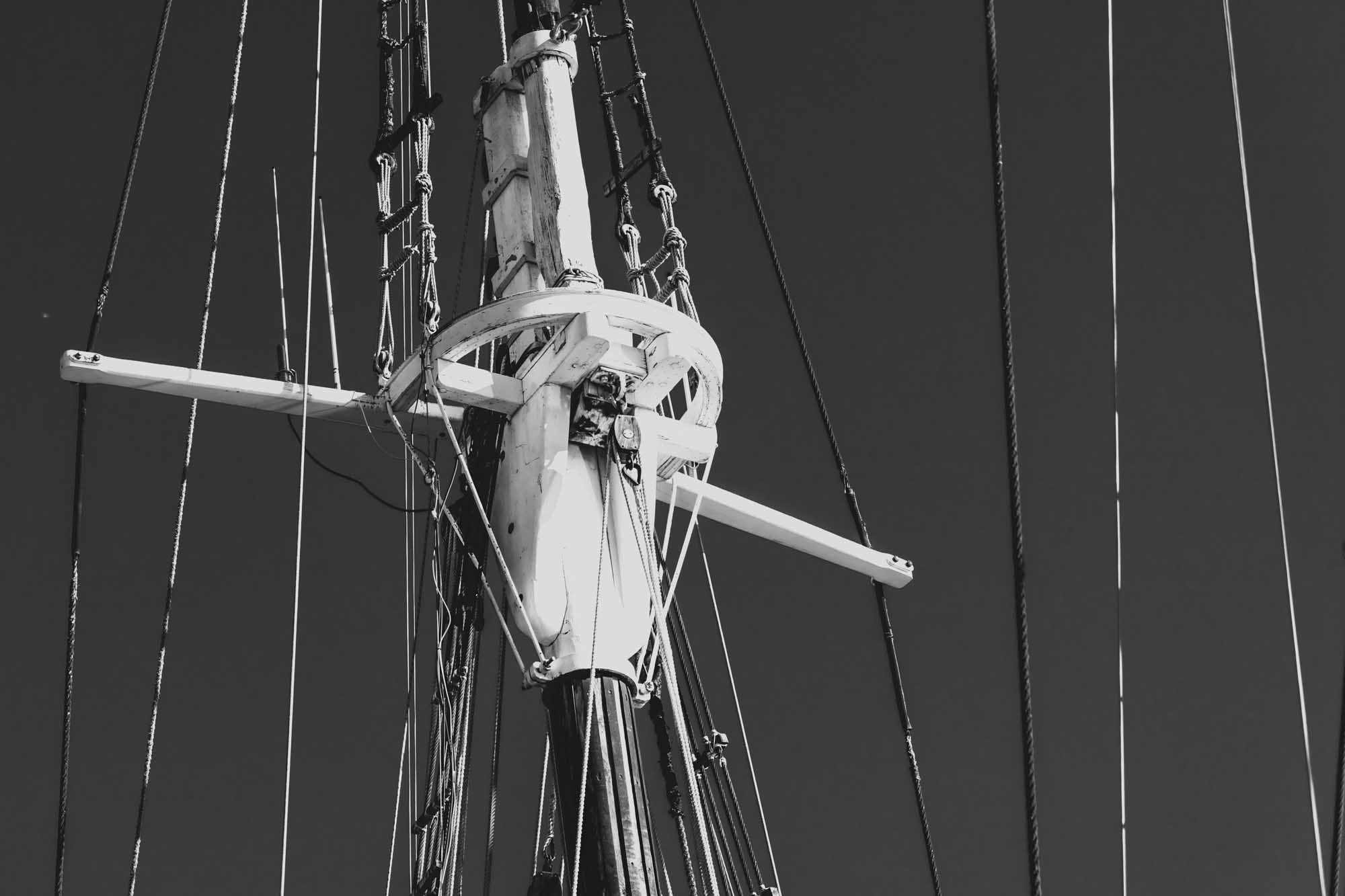 Black and white close-up of a ship mast and rigging against a clear sky.