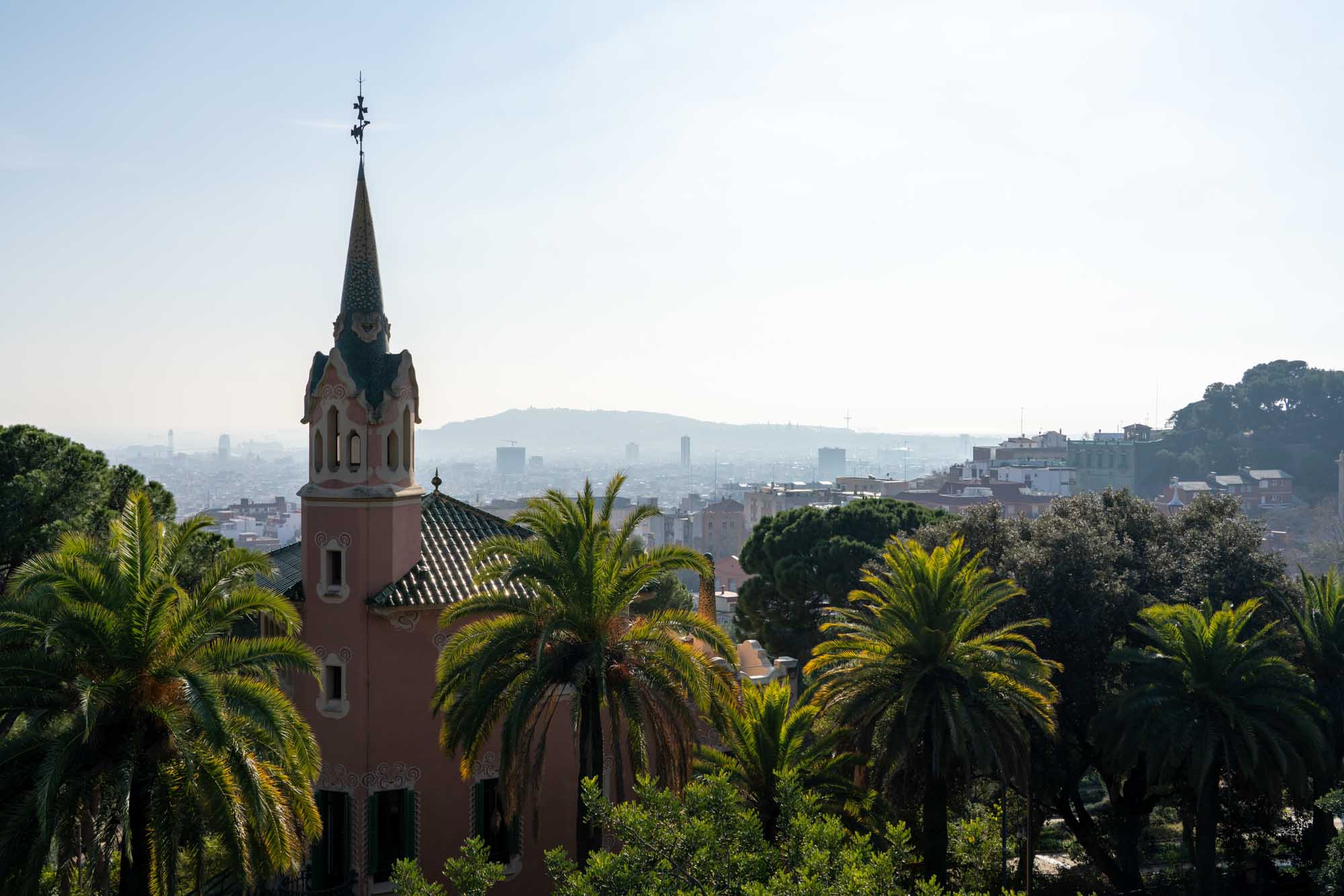 Ornate tower surrounded by palm trees overlooking a hazy cityscape under a clear sky.