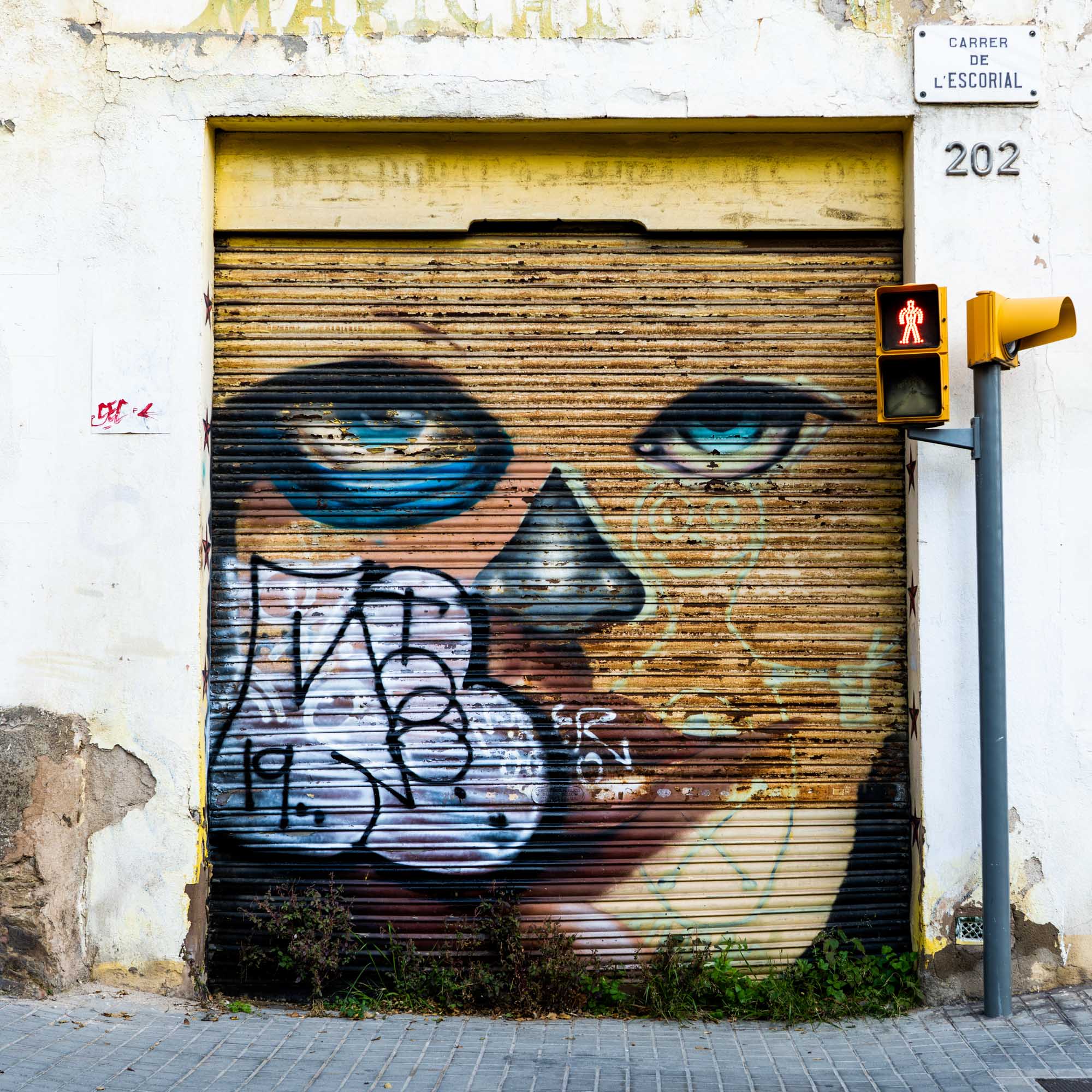 Graffiti of a woman's face with blue eyes on a shutter next to a pedestrian cross signal on a textured urban wall.
