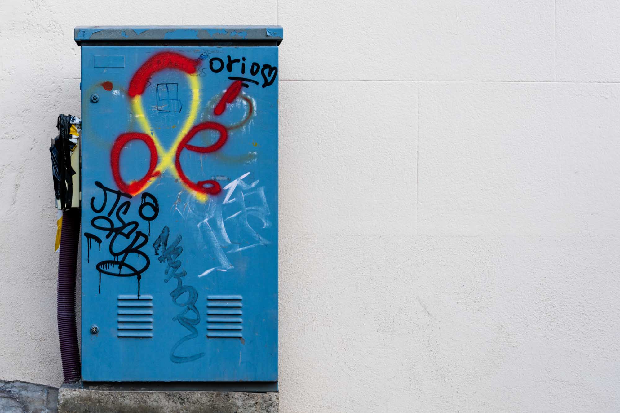 Blue utility box with colorful graffiti against a white wall. Vibrant street art in urban setting.