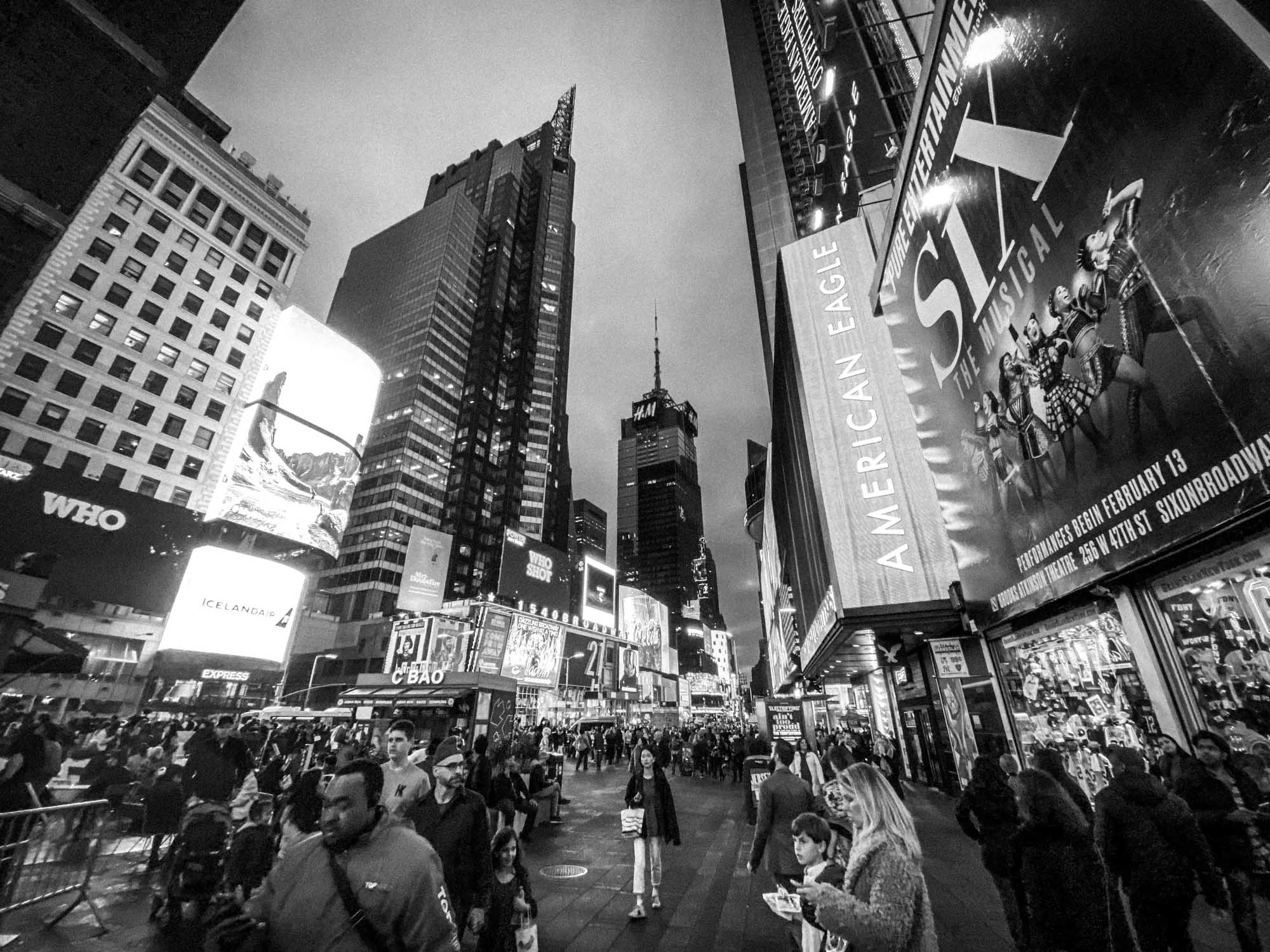 Busy Times Square at dusk with crowds and bright billboards, including Six musical and American Eagle signage.