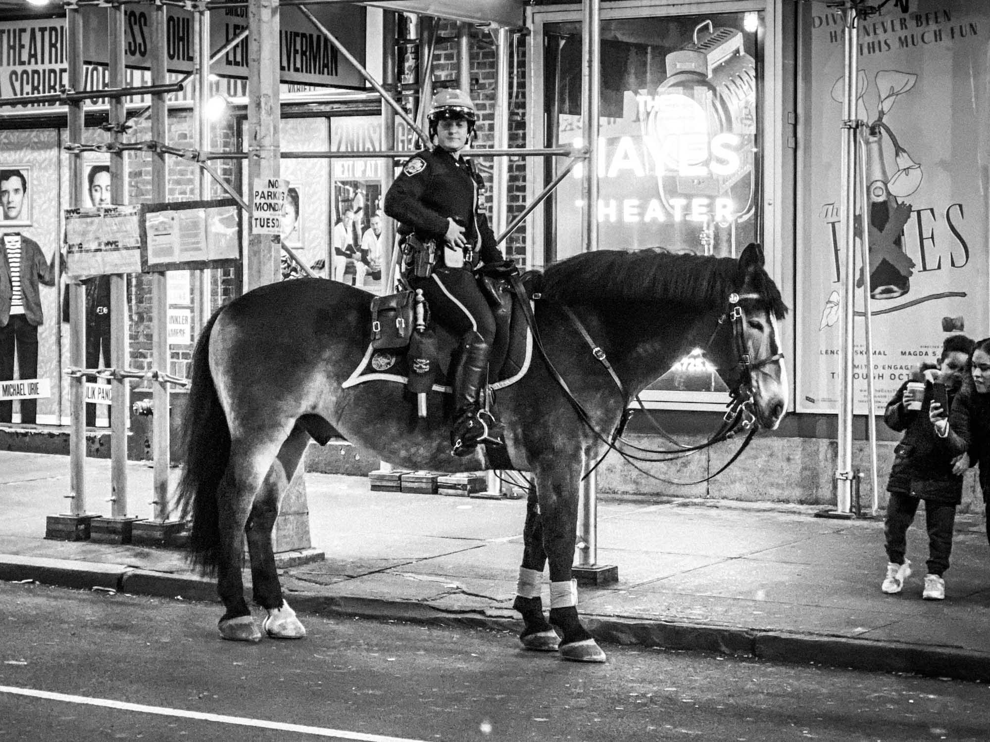 Mounted police officer on horseback by theater posters at night, capturing urban street scene.